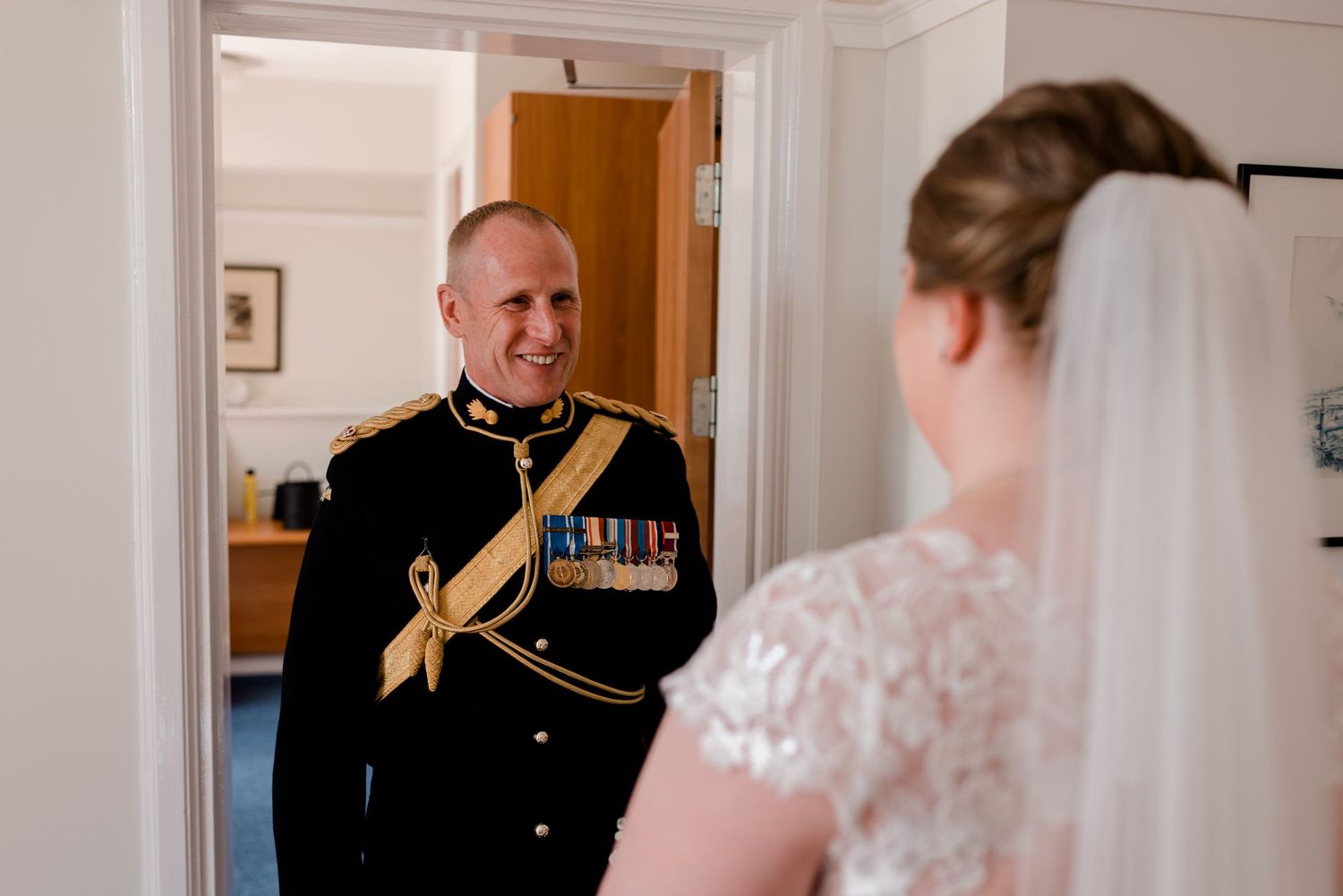 A lace-detailed wedding dress is showcased in an elegant white room with crown molding and classic decor.