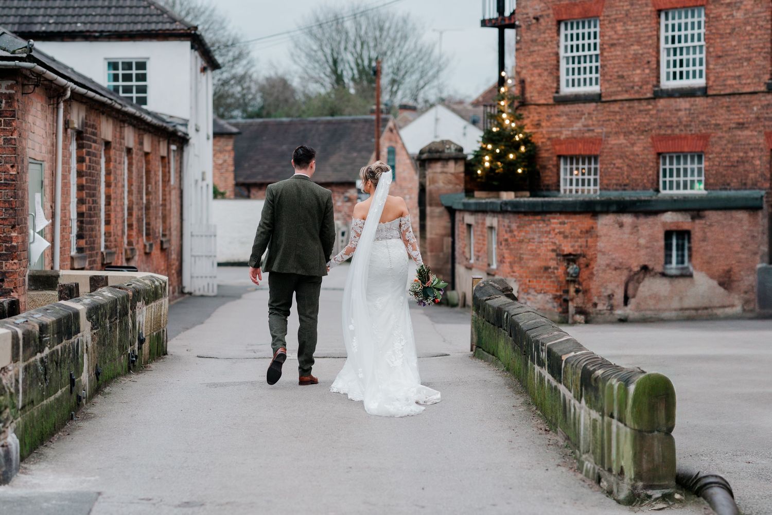 Bride and groom walk hand in hand through a charming brick courtyard on their wedding day.