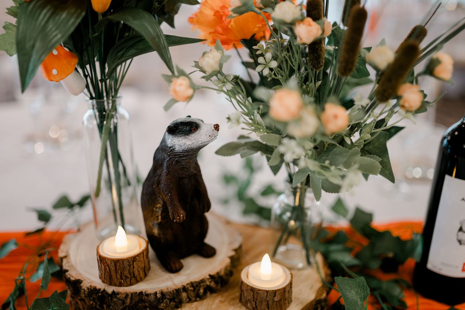 Wedding table centerpieces featuring orange flowers and candles on rustic wood slices.