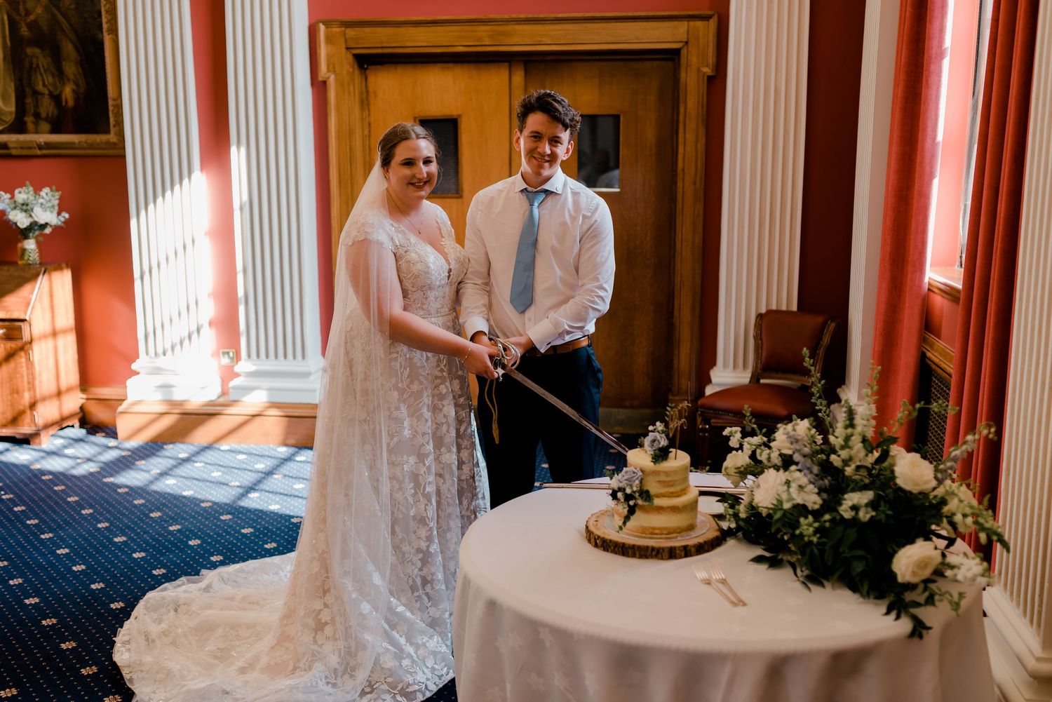 Elegant wedding couple shares a joyful moment while cutting their rustic naked cake at their celebration.