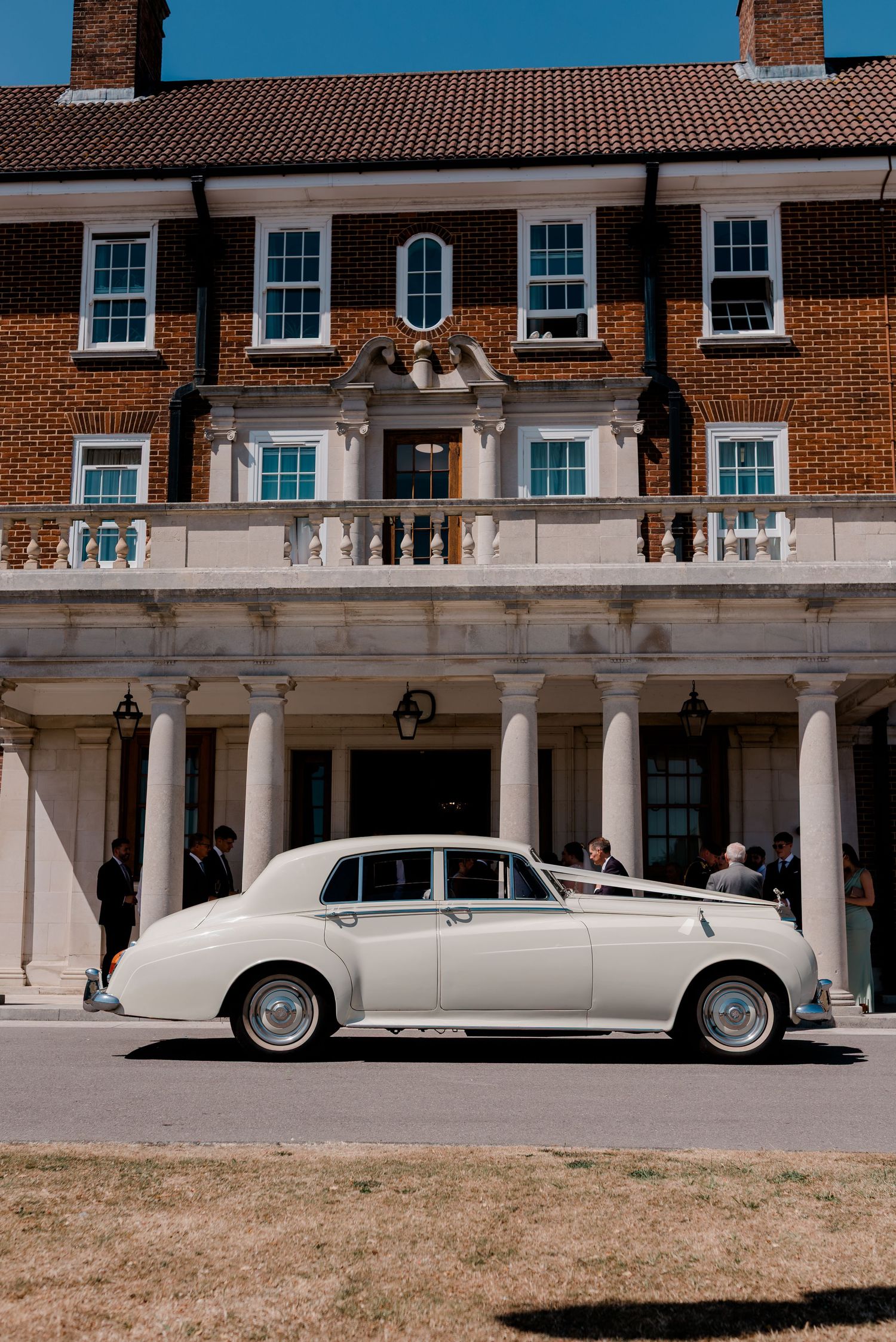 Three views of a classic white Rolls-Royce limousine parked in front of a grand brick colonial building.