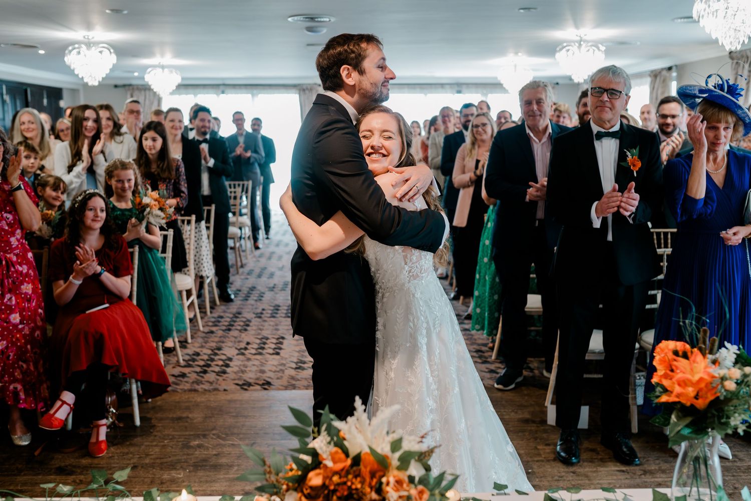 Wedding guests celebrate and dance together in an elegant reception hall with crystal chandeliers.