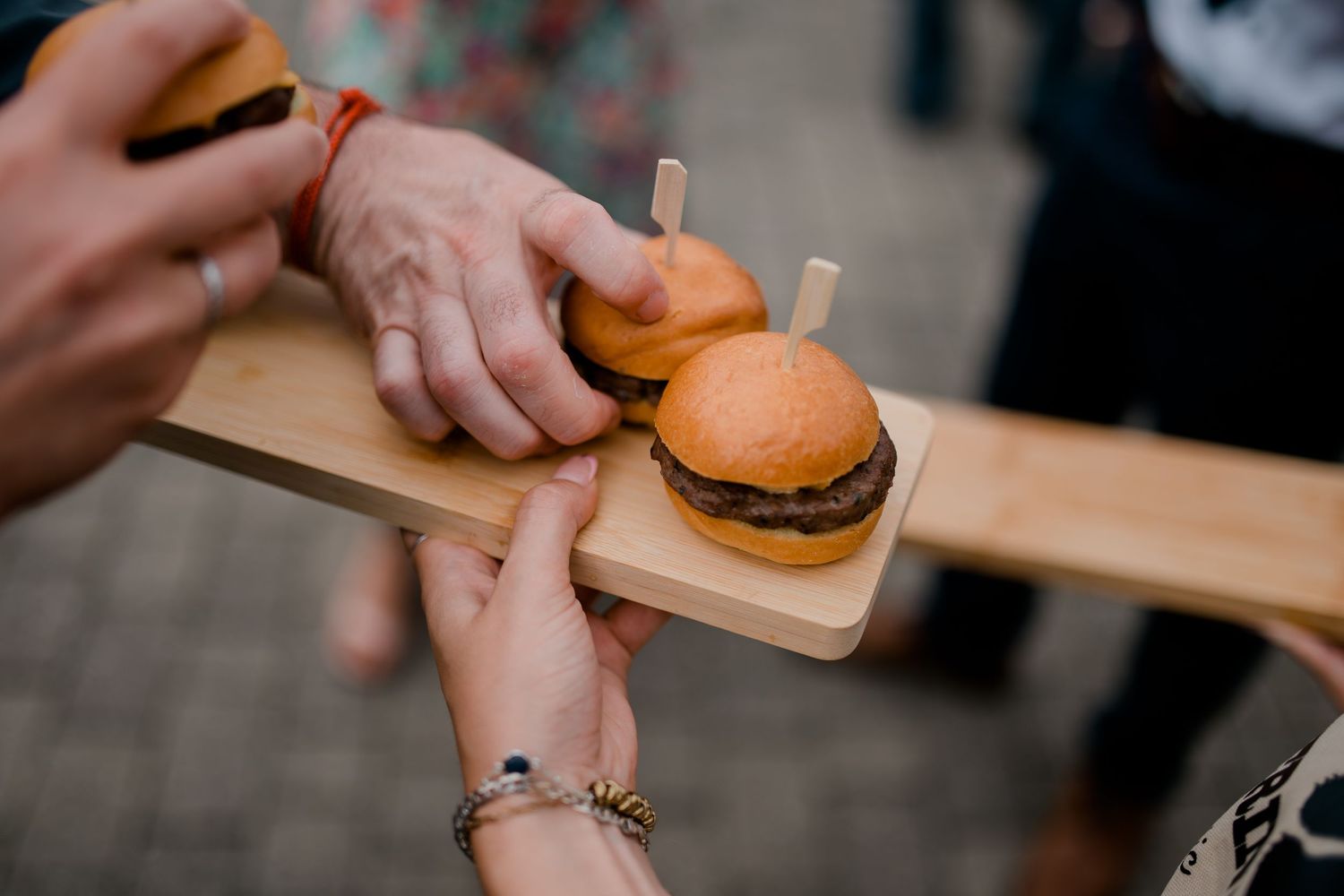 Hands holding a classic cheeseburger on a wooden serving board.