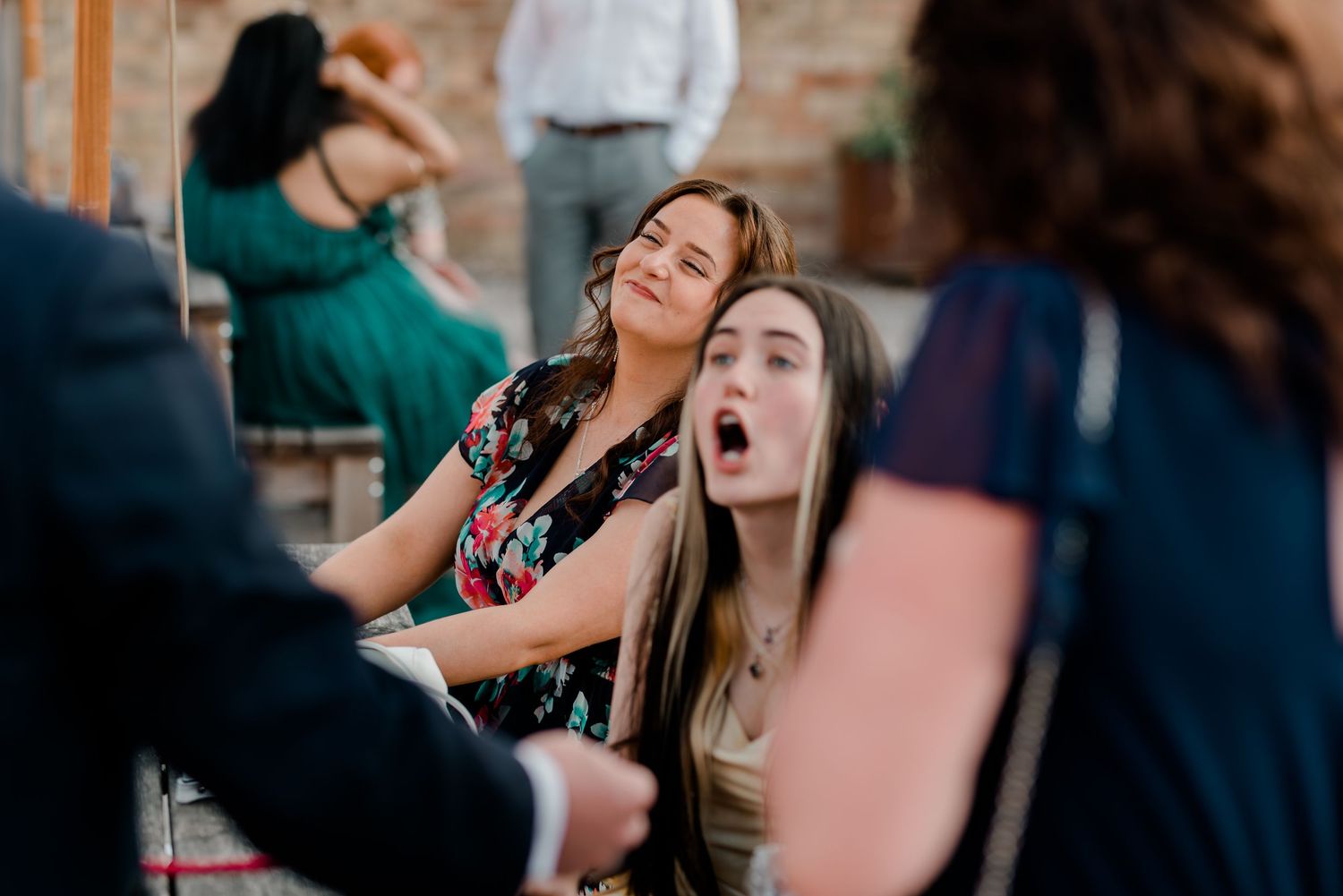 Wedding guests laughing and enjoying themselves at an outdoor reception with brick building backdrop.