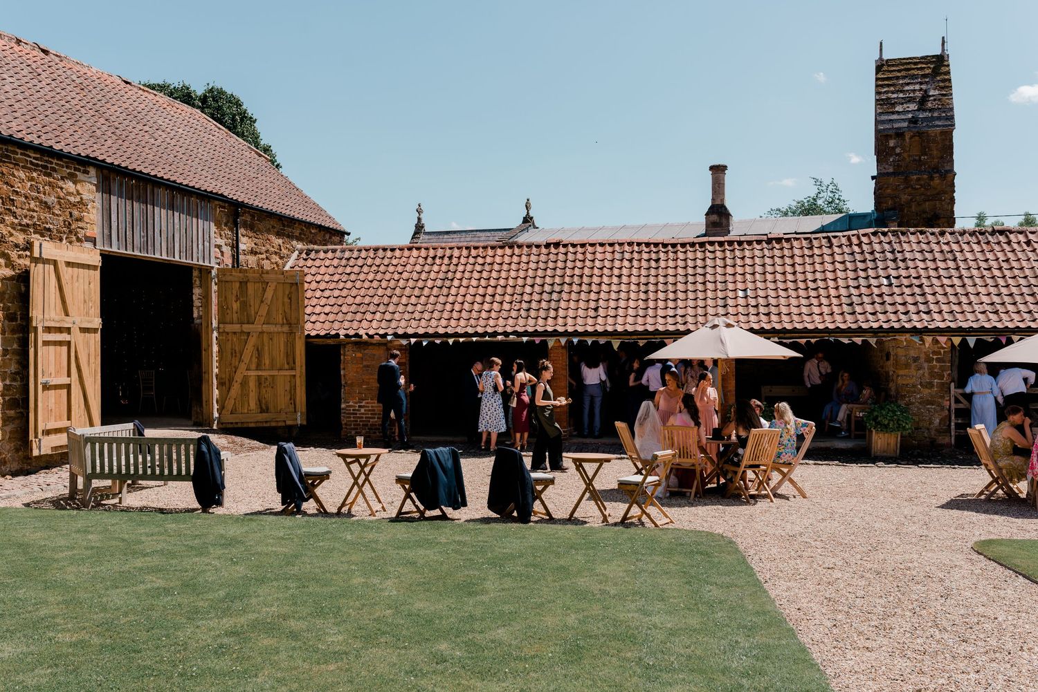 Rustic outdoor venue setup with wooden folding chairs arranged on a stone patio against barn buildings.
