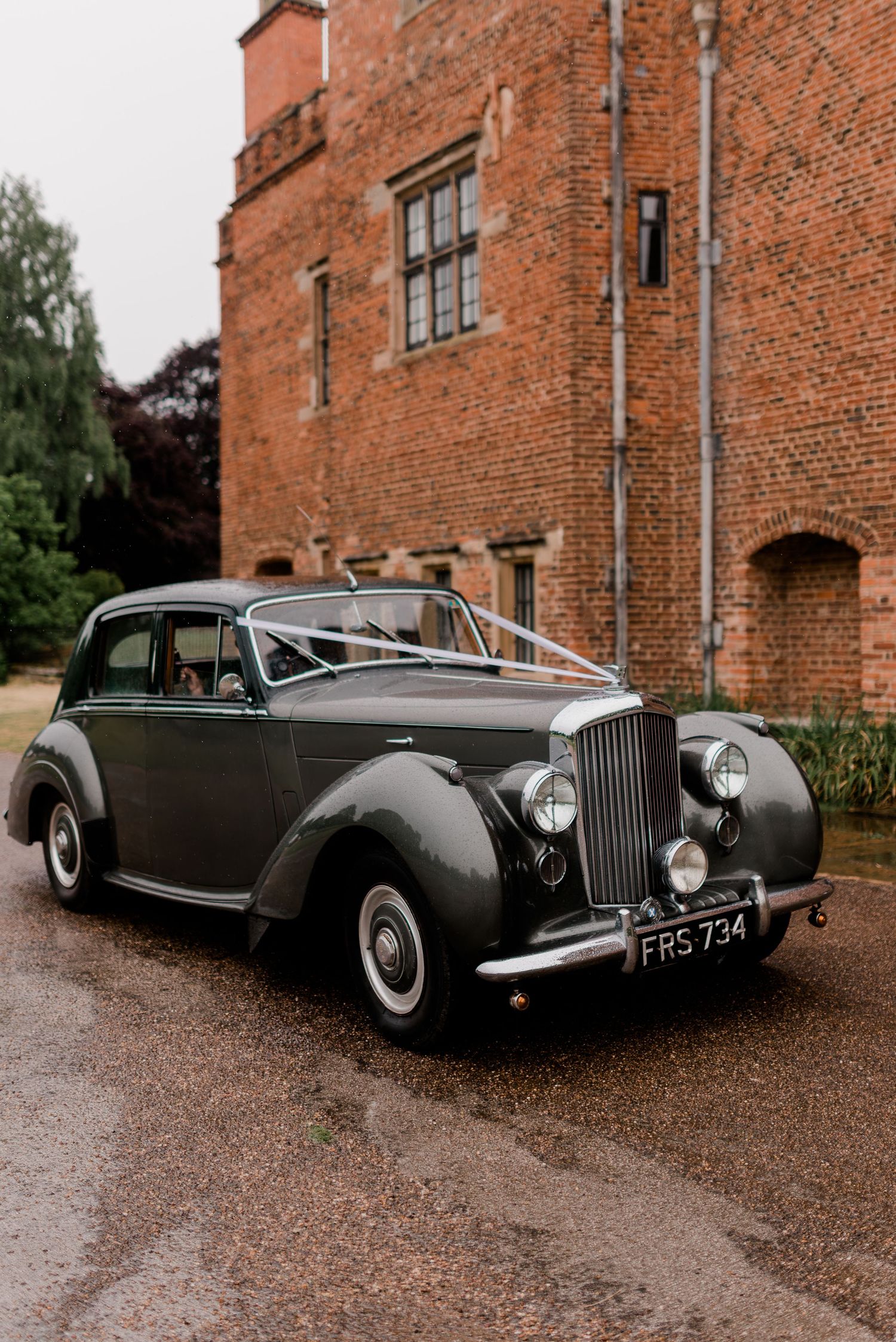 Vintage Rolls-Royce cars displayed in front of a historic red brick manor building.