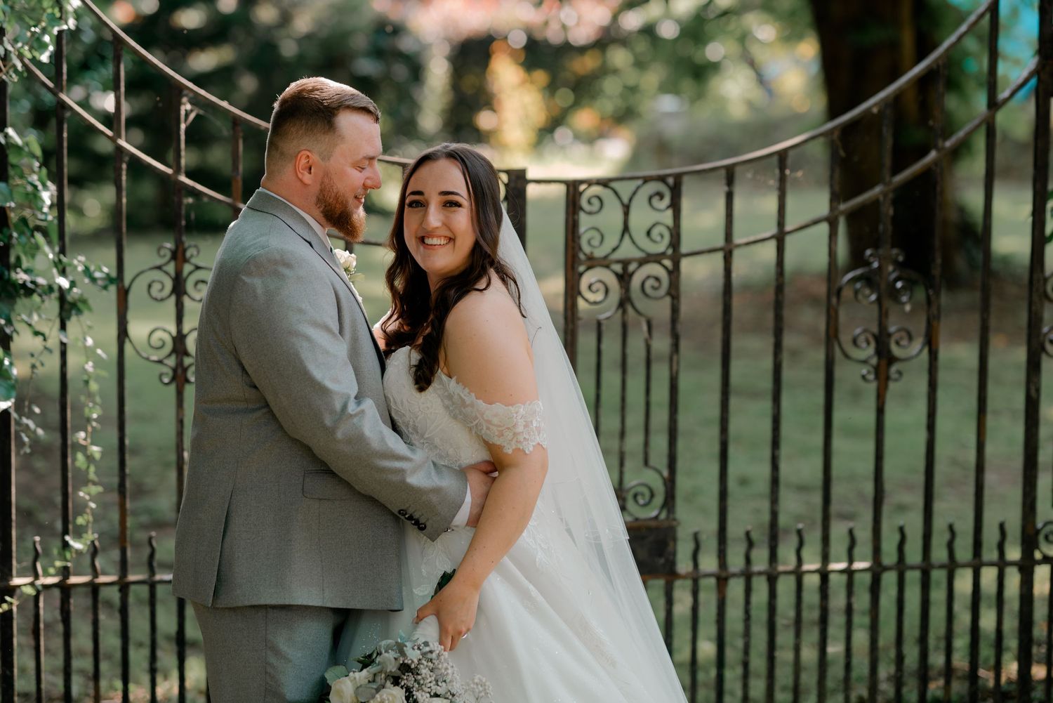 Newlyweds share joyful embraces while posing for photos near a decorative black iron fence.