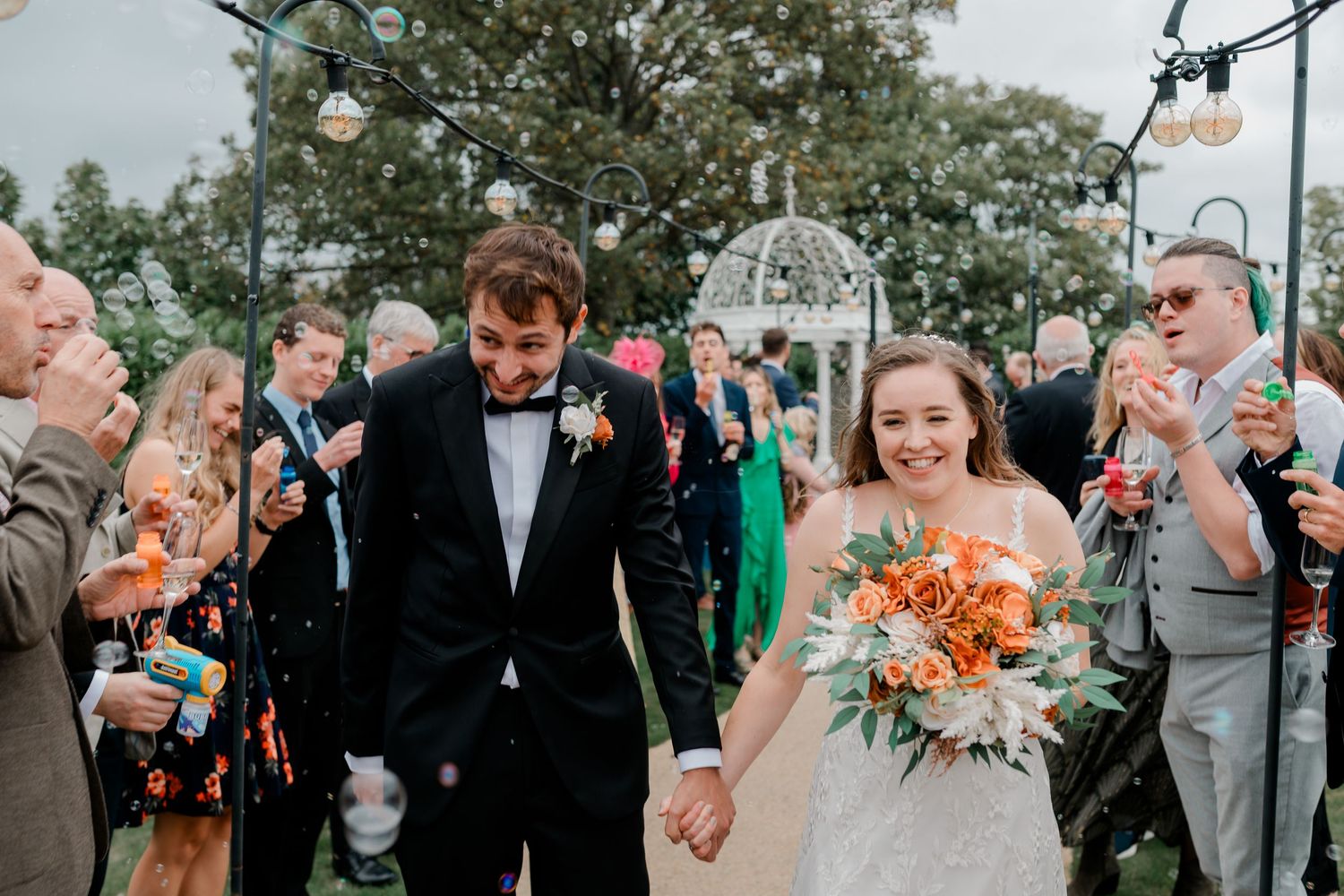 Wedding party celebrating outdoors with orange flowers and formal attire at daytime celebration.
