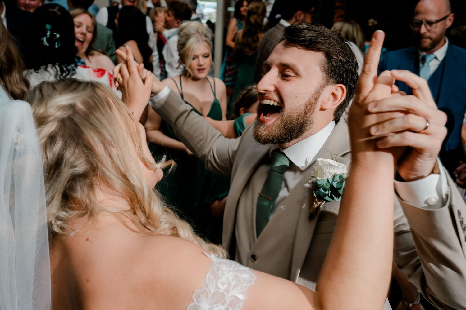 Bride and groom sing and dance together joyfully on wedding reception dance floor with guests.