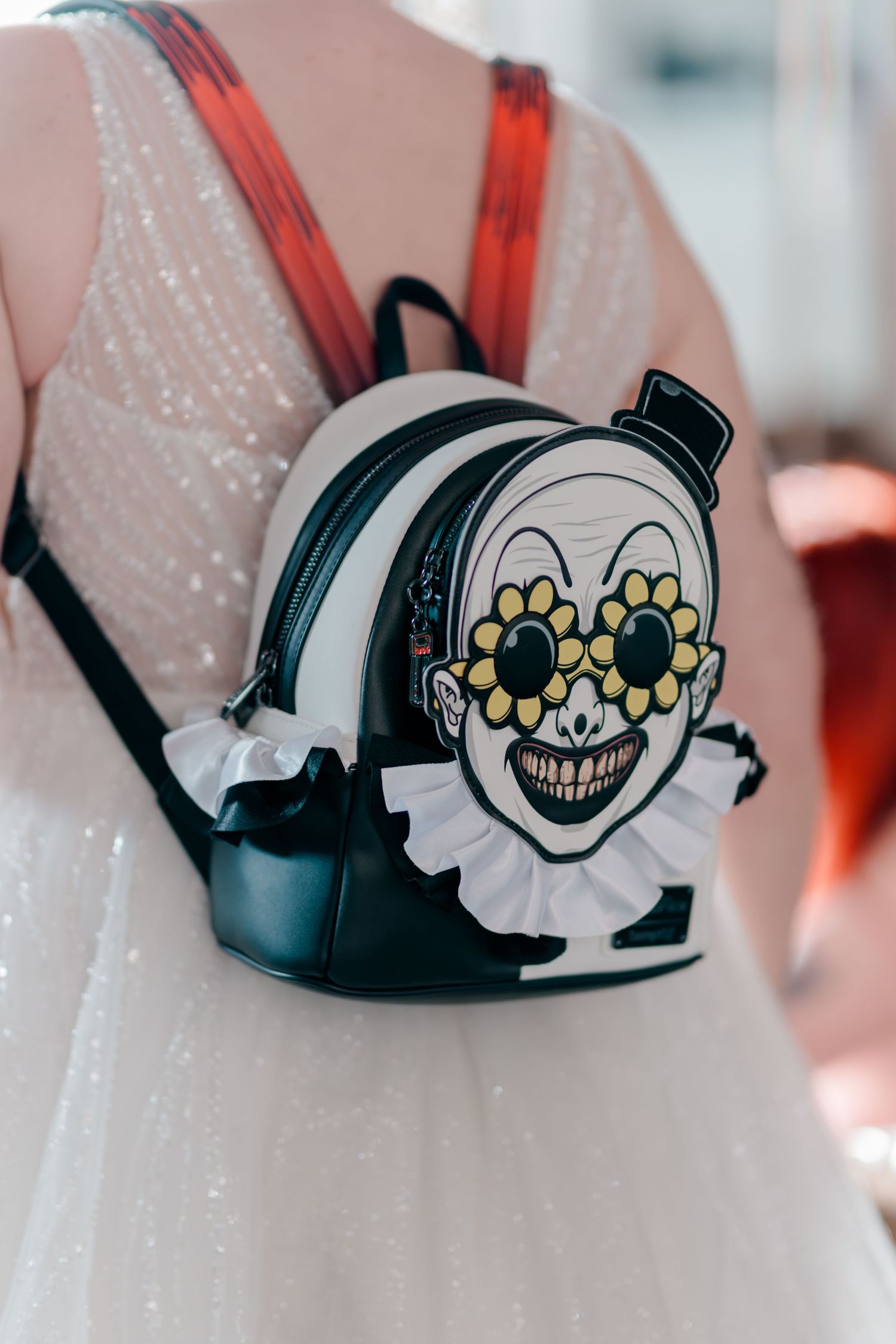 White sequin dress with clown face mini backpack featuring flower sunglasses and ruffled collar detail.