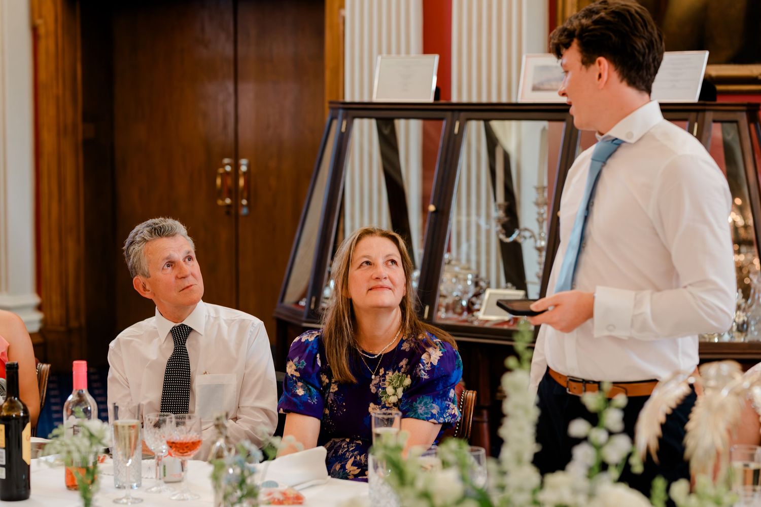 Wedding guests celebrate at an elegant reception with wine glasses and decorative candles on long dining tables.
