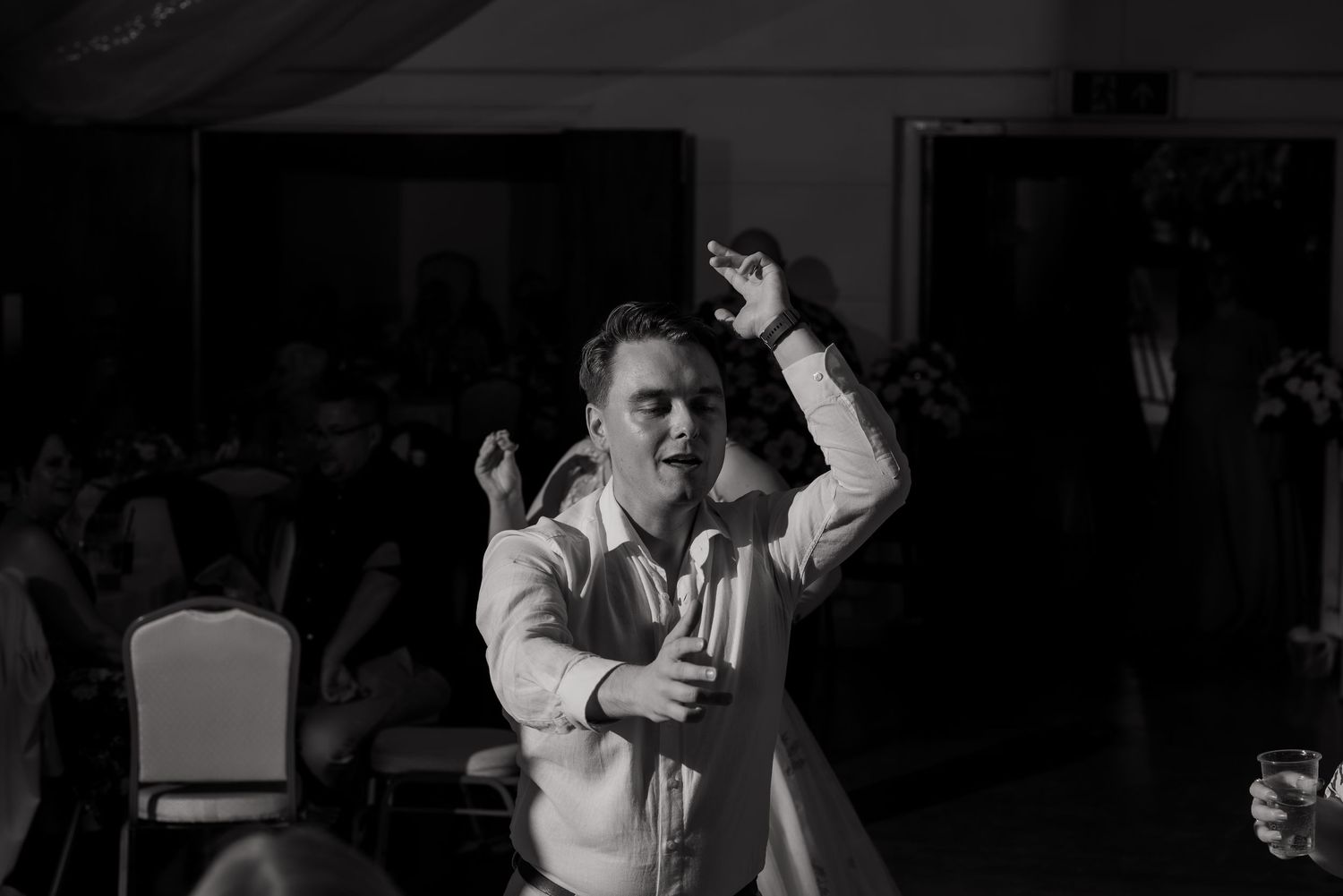 Wedding reception dance party with guests celebrating in dark venue with ambient lighting.