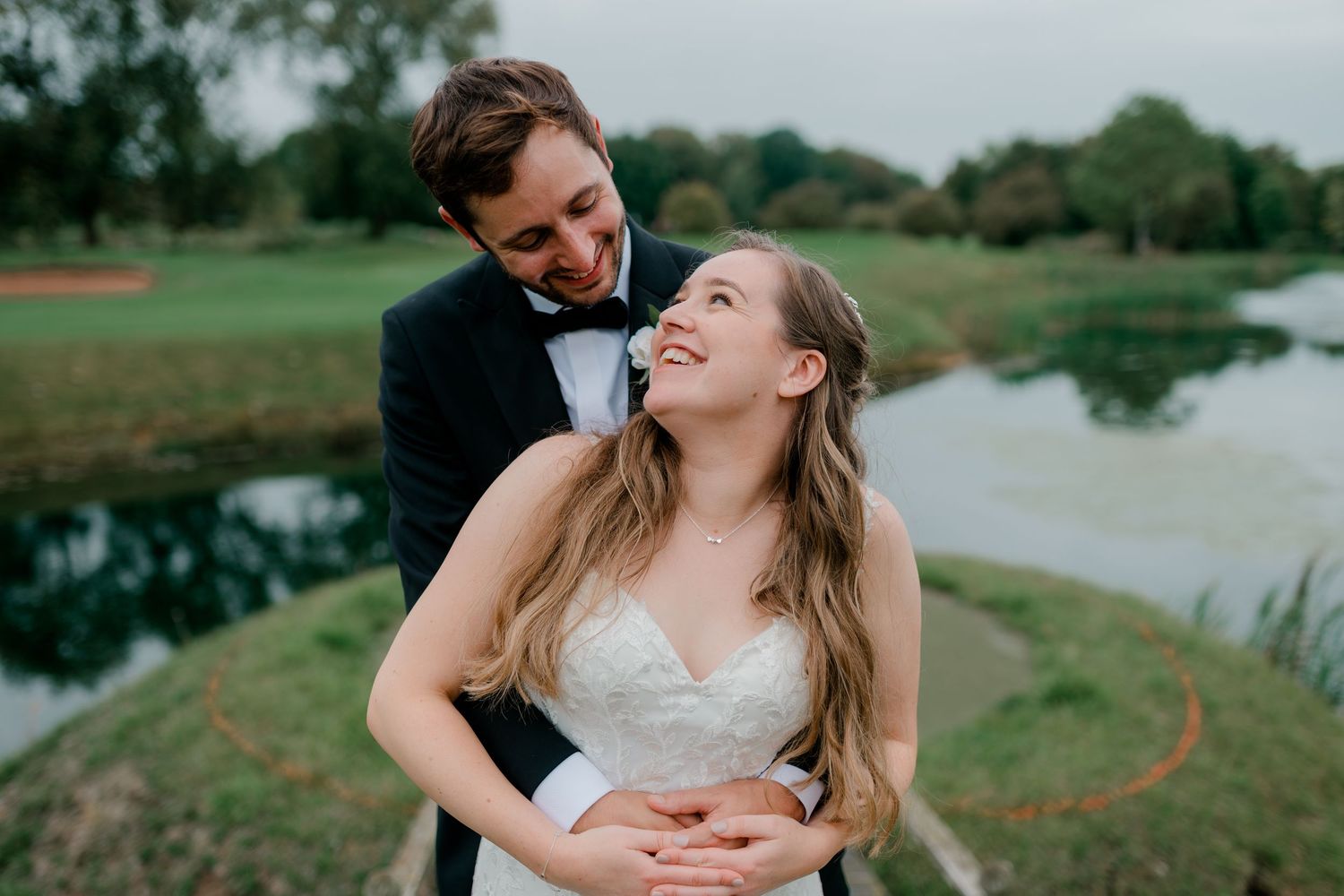 A couple shares an intimate moment on a golf course with a lake in the background during sunset.