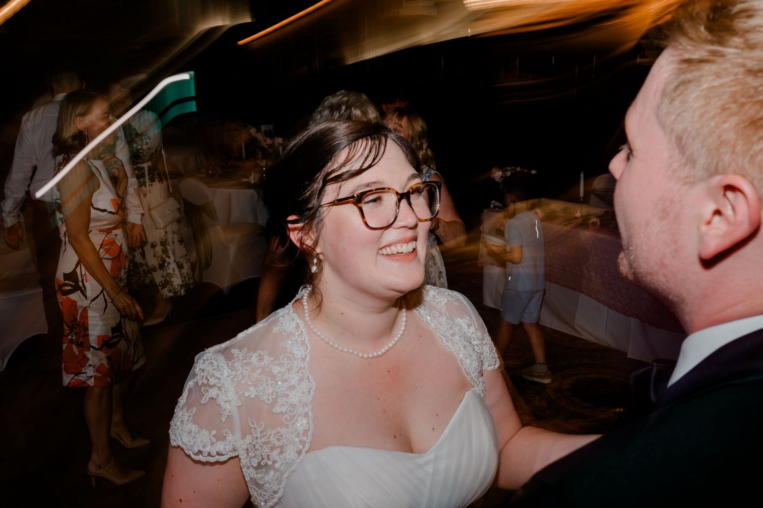 Bride in lace wedding dress smiling and dancing with her groom at their wedding reception.