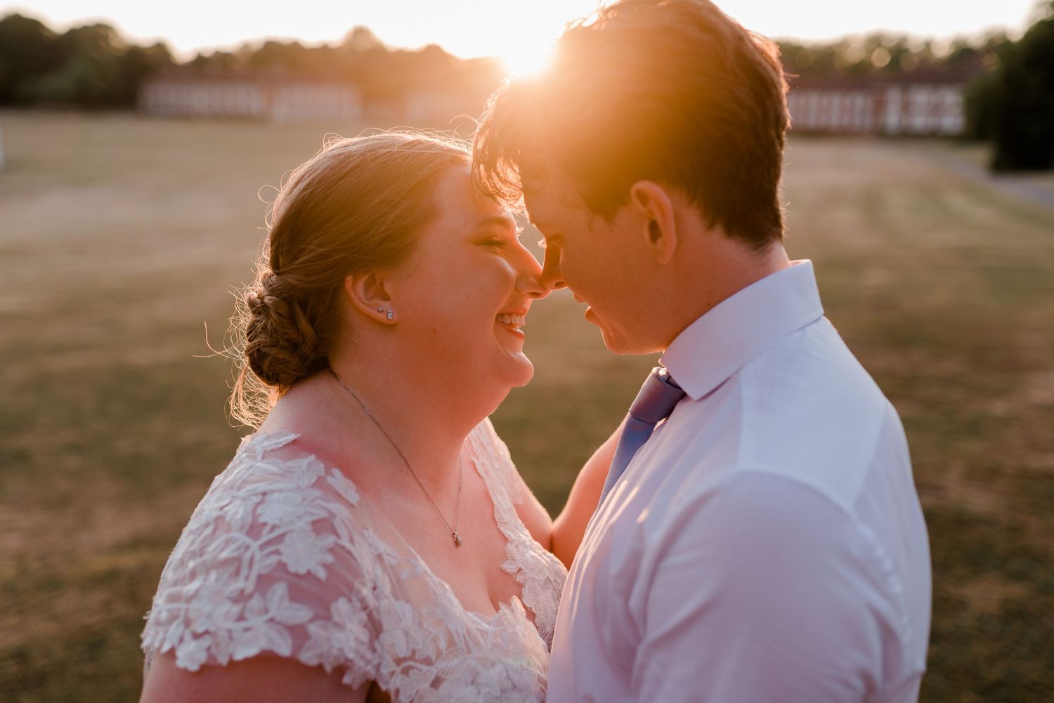 Bride and groom share a joyful forehead touch bathed in warm golden sunset light.