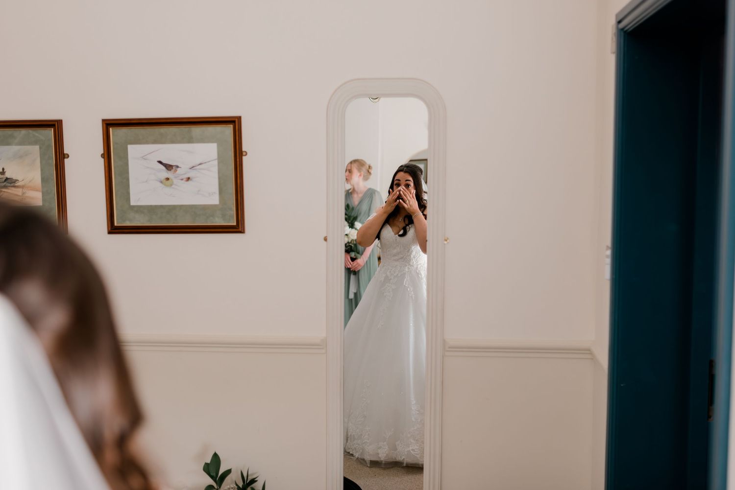 Indoor bridal preparation scene with natural window light in a minimalist room with framed artwork.