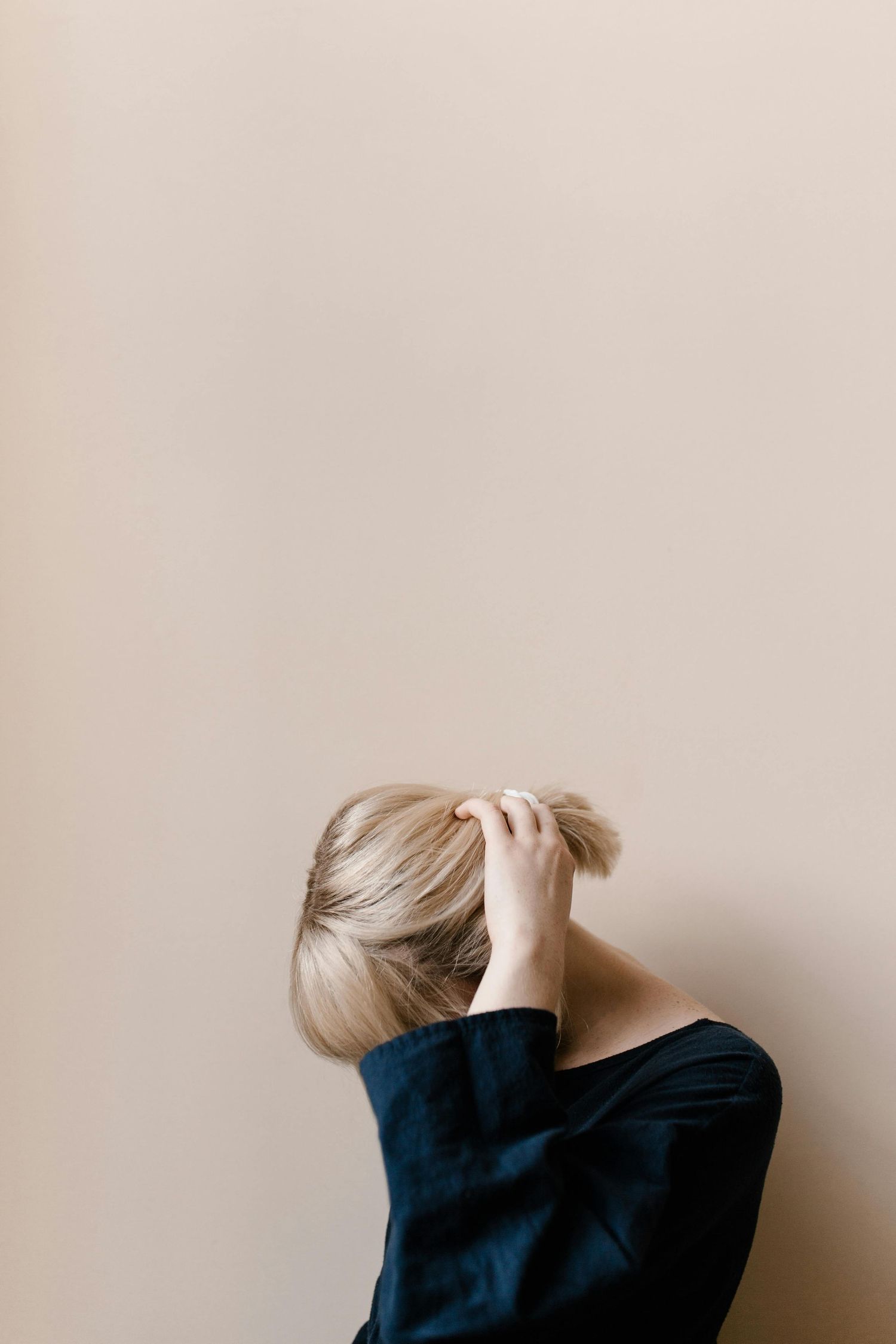 Artistic portrait of blonde person in navy top against beige wall.