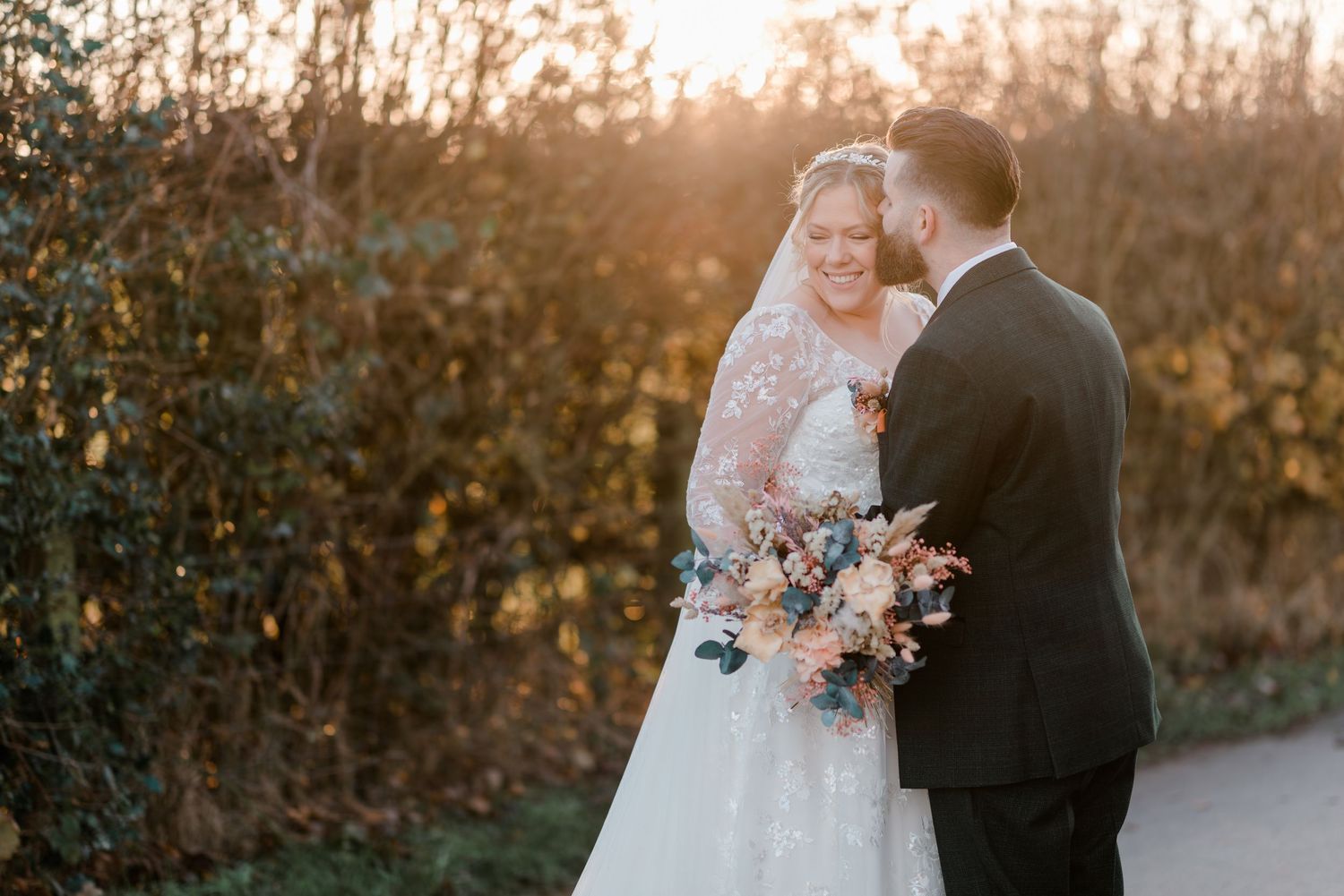 Bride and groom embracing in warm golden sunset light with bride holding colorful autumn wedding bouquet.