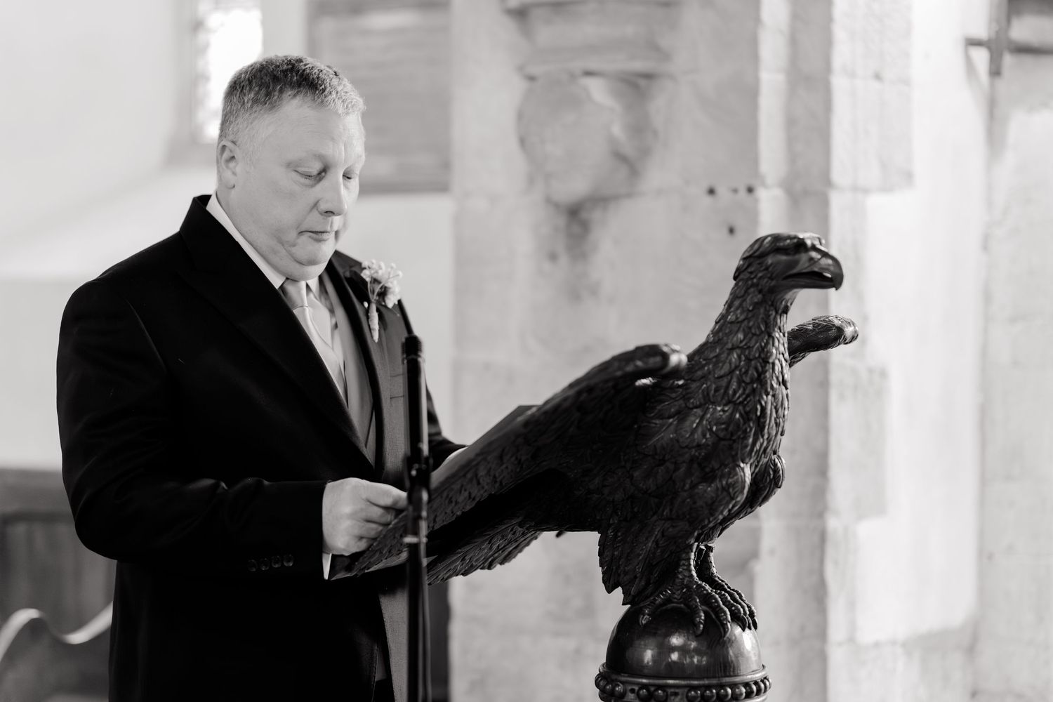 Man in black suit reading from an eagle lectern inside a church during a wedding ceremony.