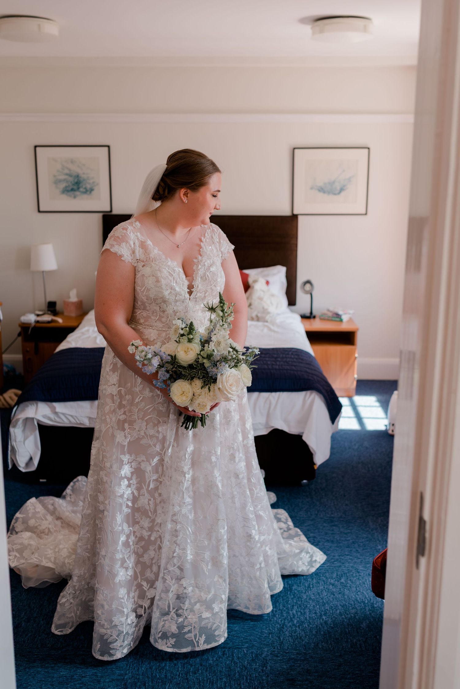 White lace wedding dress laid out on blue carpeted floor in elegant hotel room interior.