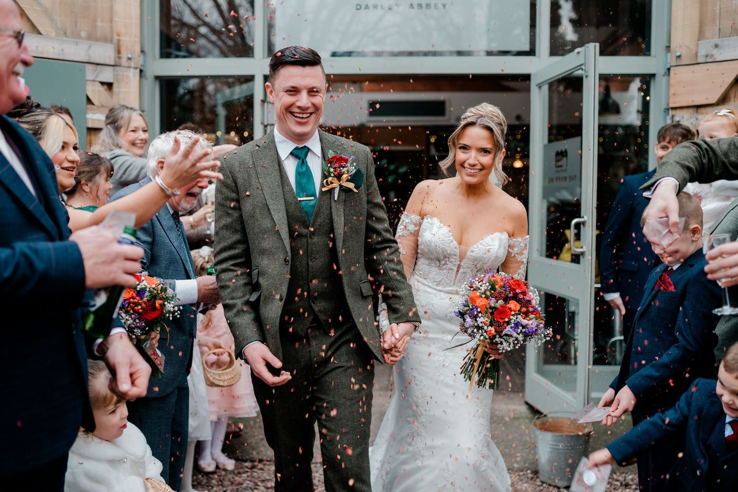 Bride and groom exit venue hand in hand through a shower of colorful confetti from guests.