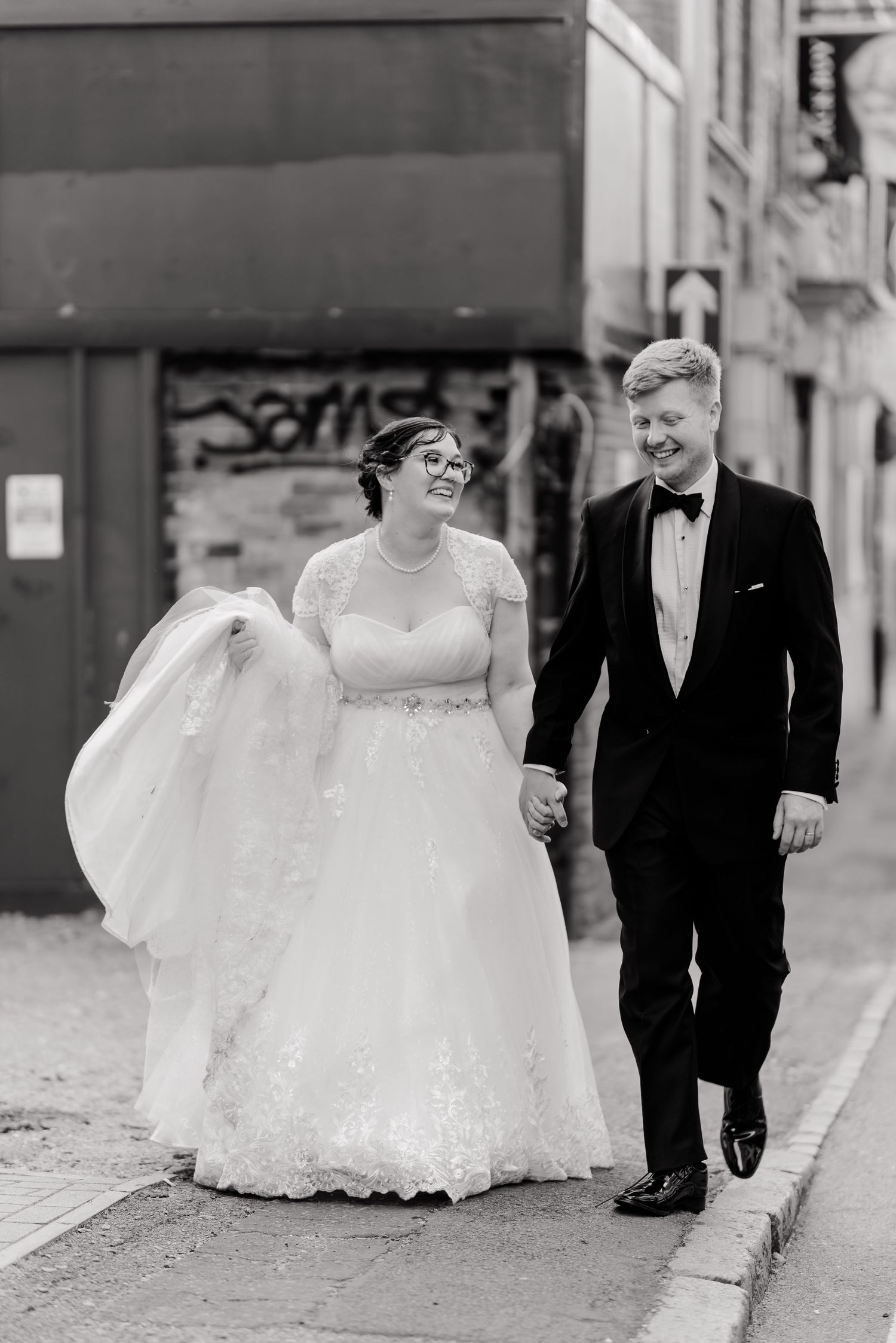 Black and white photo of a bride and groom holding hands walking down a city street on their wedding day.