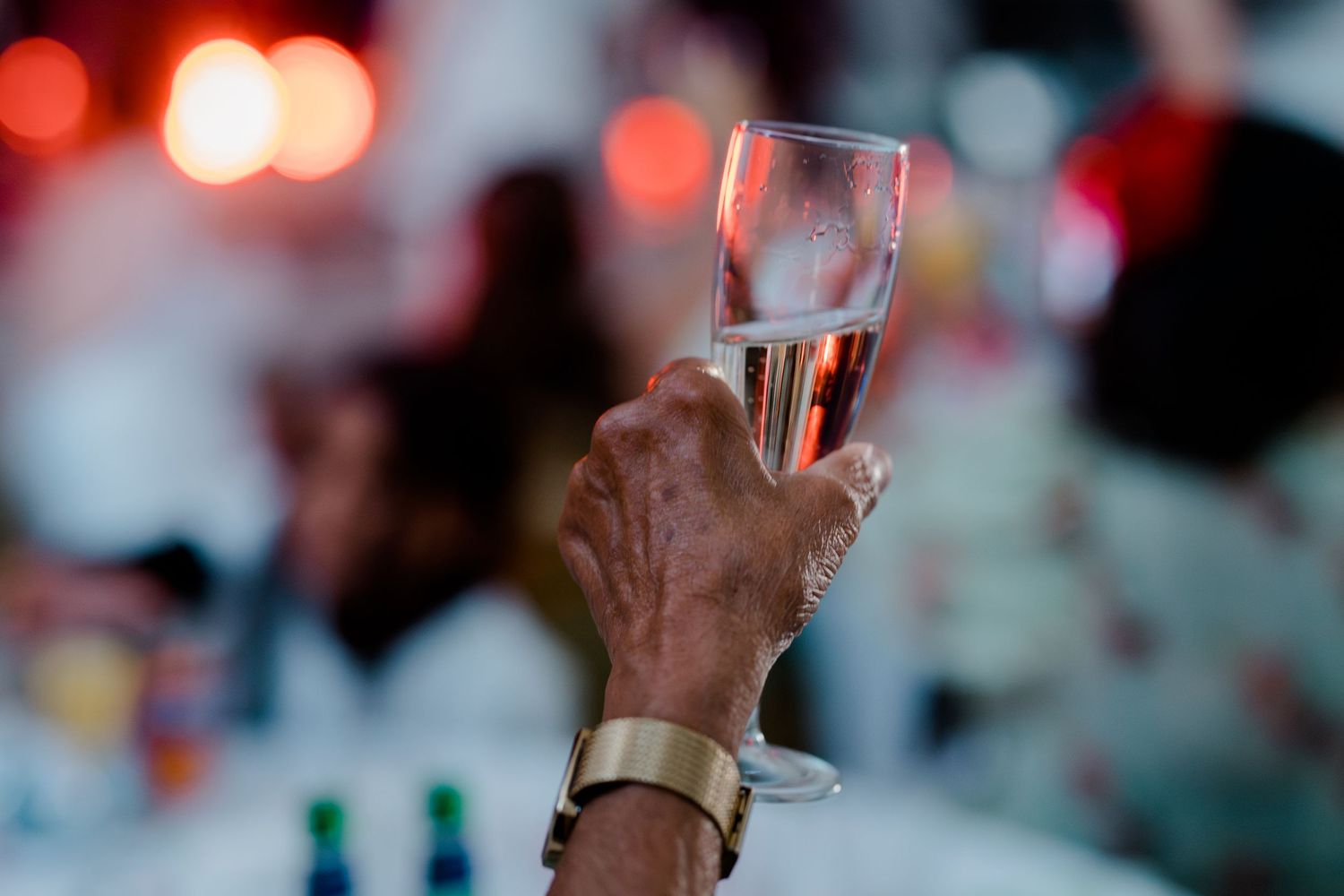 Hand raising a champagne glass in a toast at a wedding reception with bokeh lights in background.