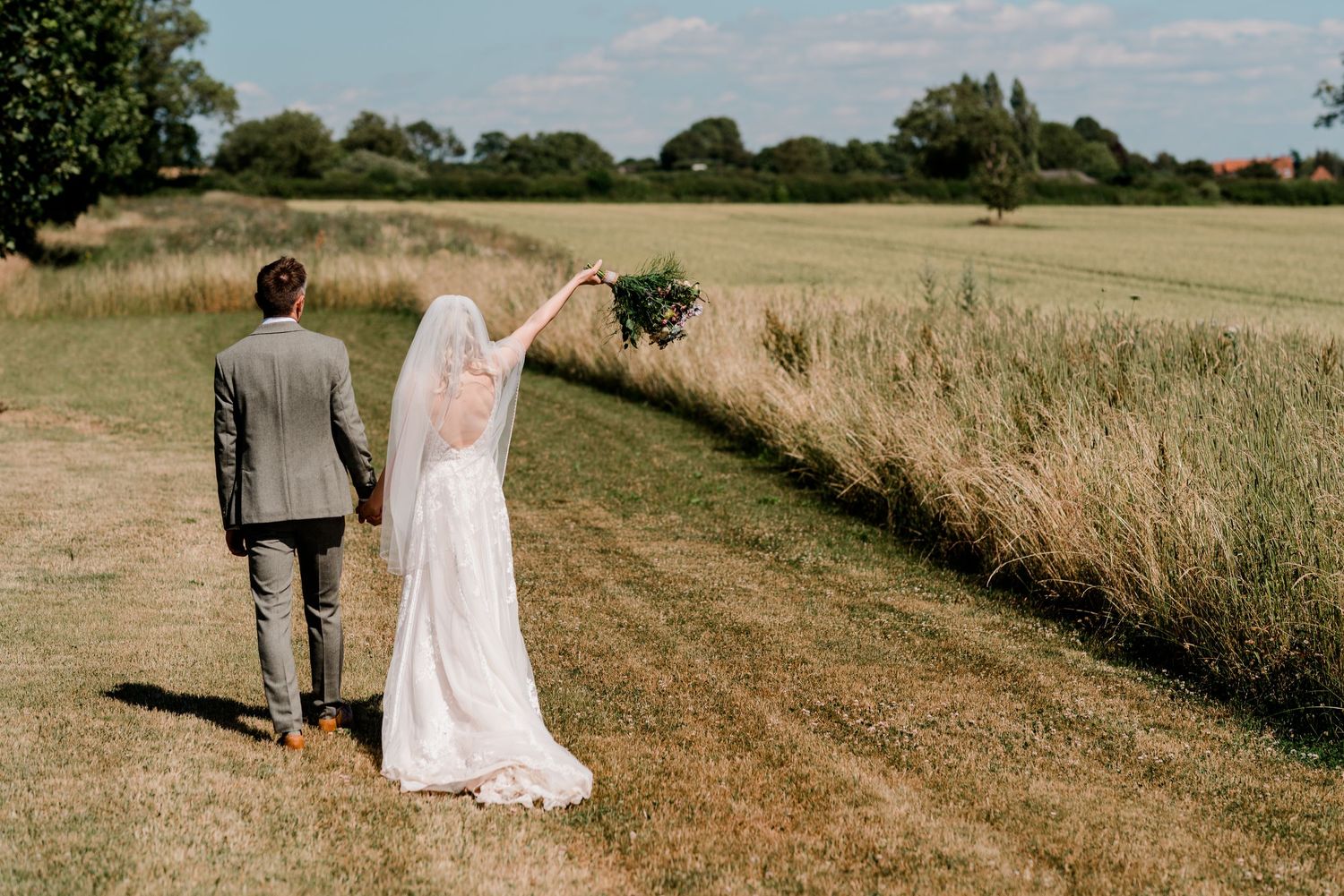 Couple walks along a scenic rural path through golden wheat fields on a bright summer day.