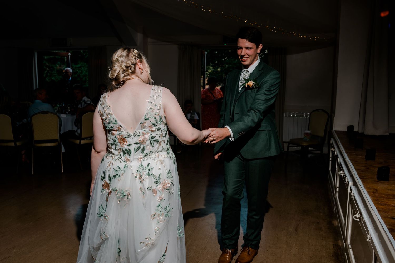 Couple dancing in an elegant ballroom with floral dress and dark suit.