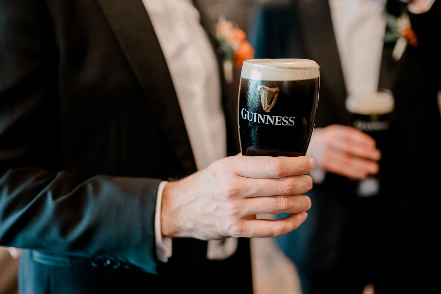 People holding and enjoying Guinness beers at a bar with copper pendant lights overhead.