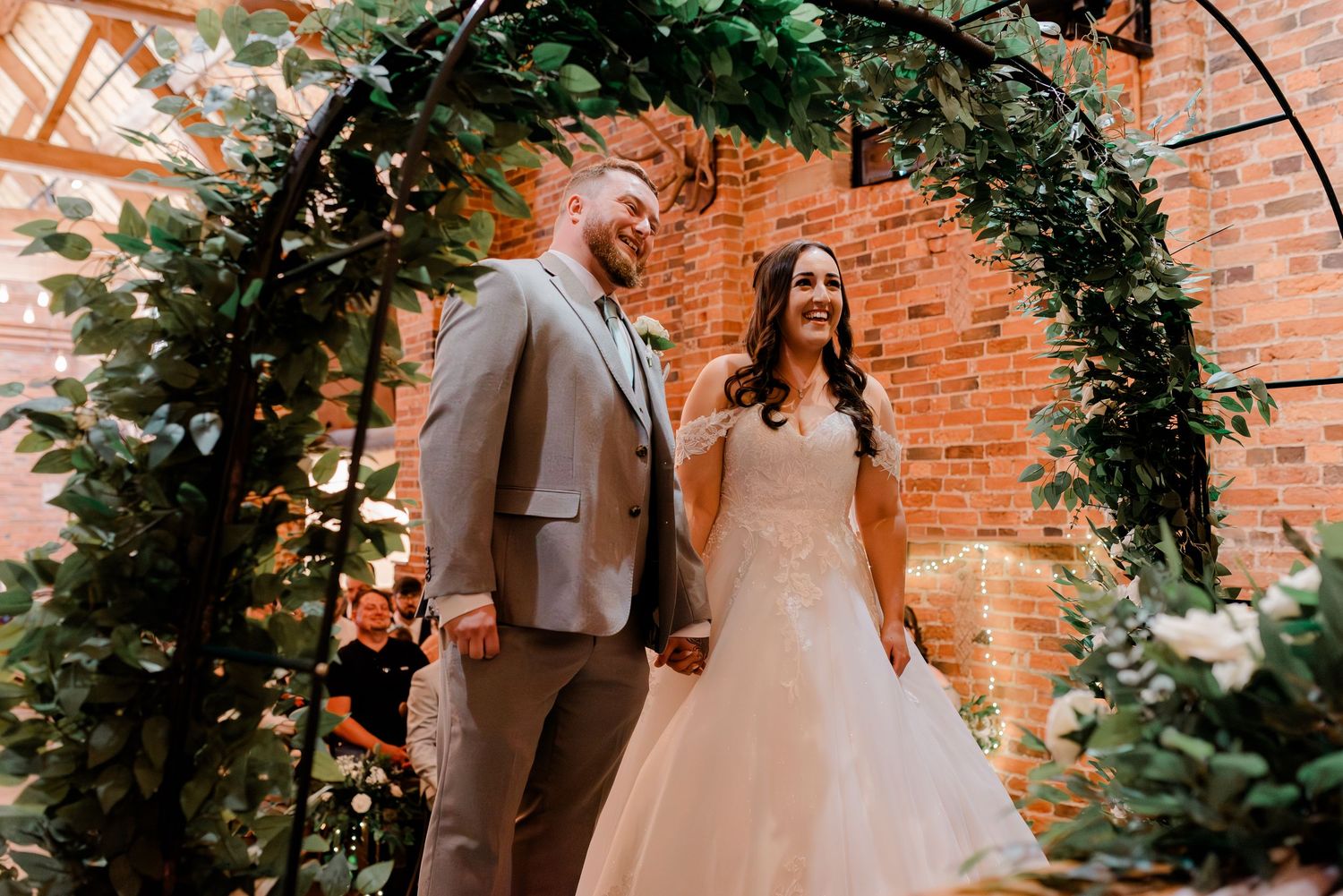 Wedding ceremony setup with lush greenery arch and exposed brick walls.