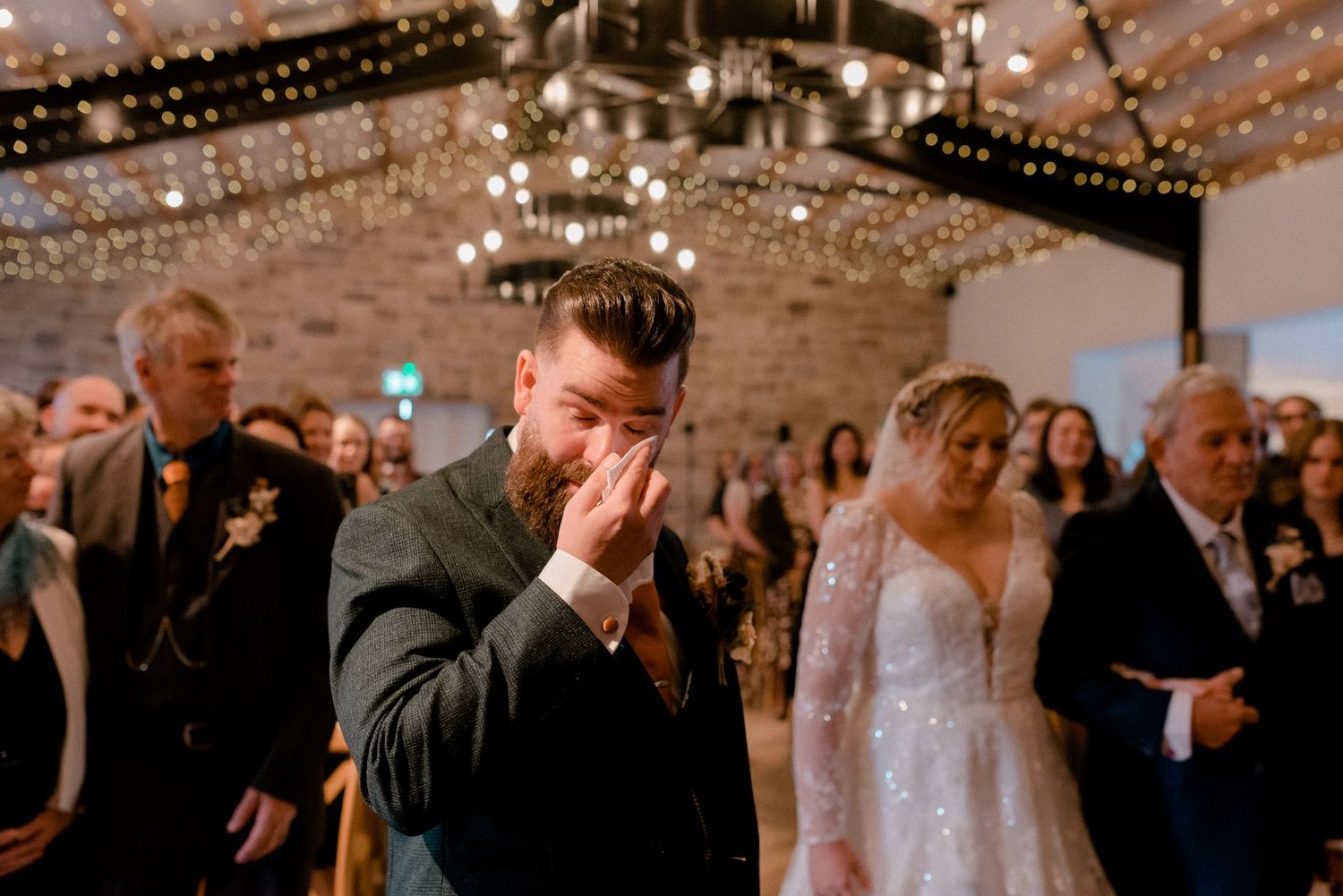 An emotional moment during a wedding reception under sparkling chandeliers and string lights.