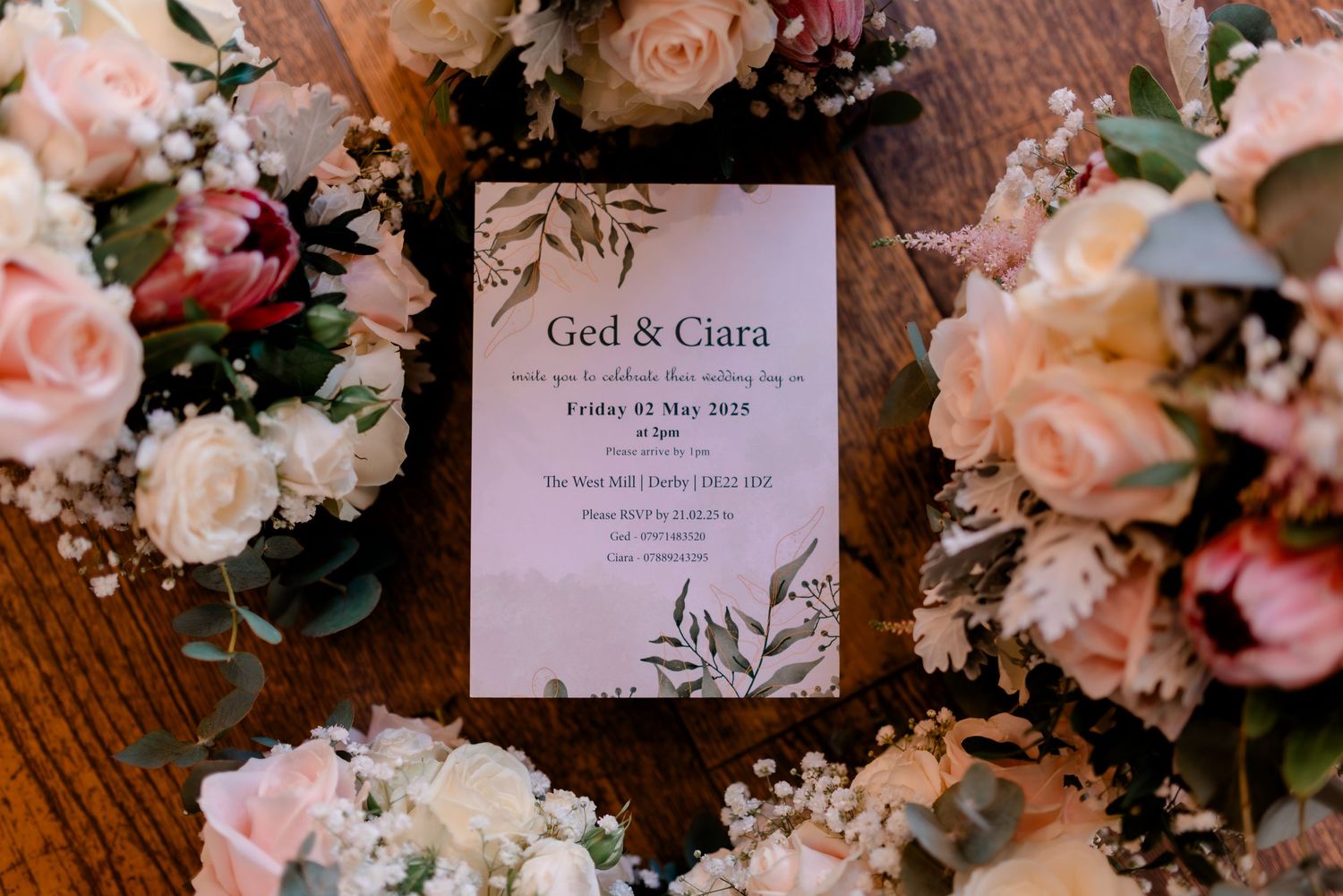 Wedding invitation suite with delicate floral design and pink roses on wooden surface.