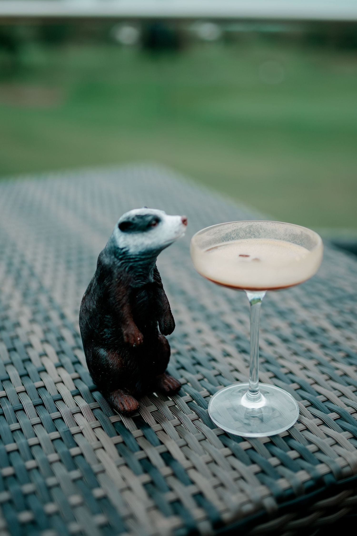 A black bird figurine sits next to a champagne cocktail on a woven outdoor table surface.