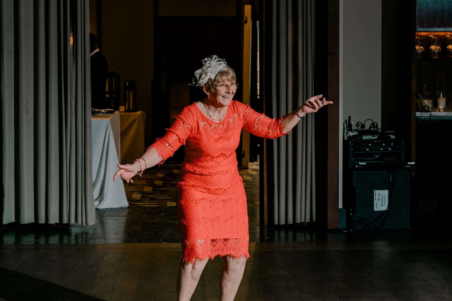 Elegant woman in coral lace dress dances joyfully at a wedding reception.