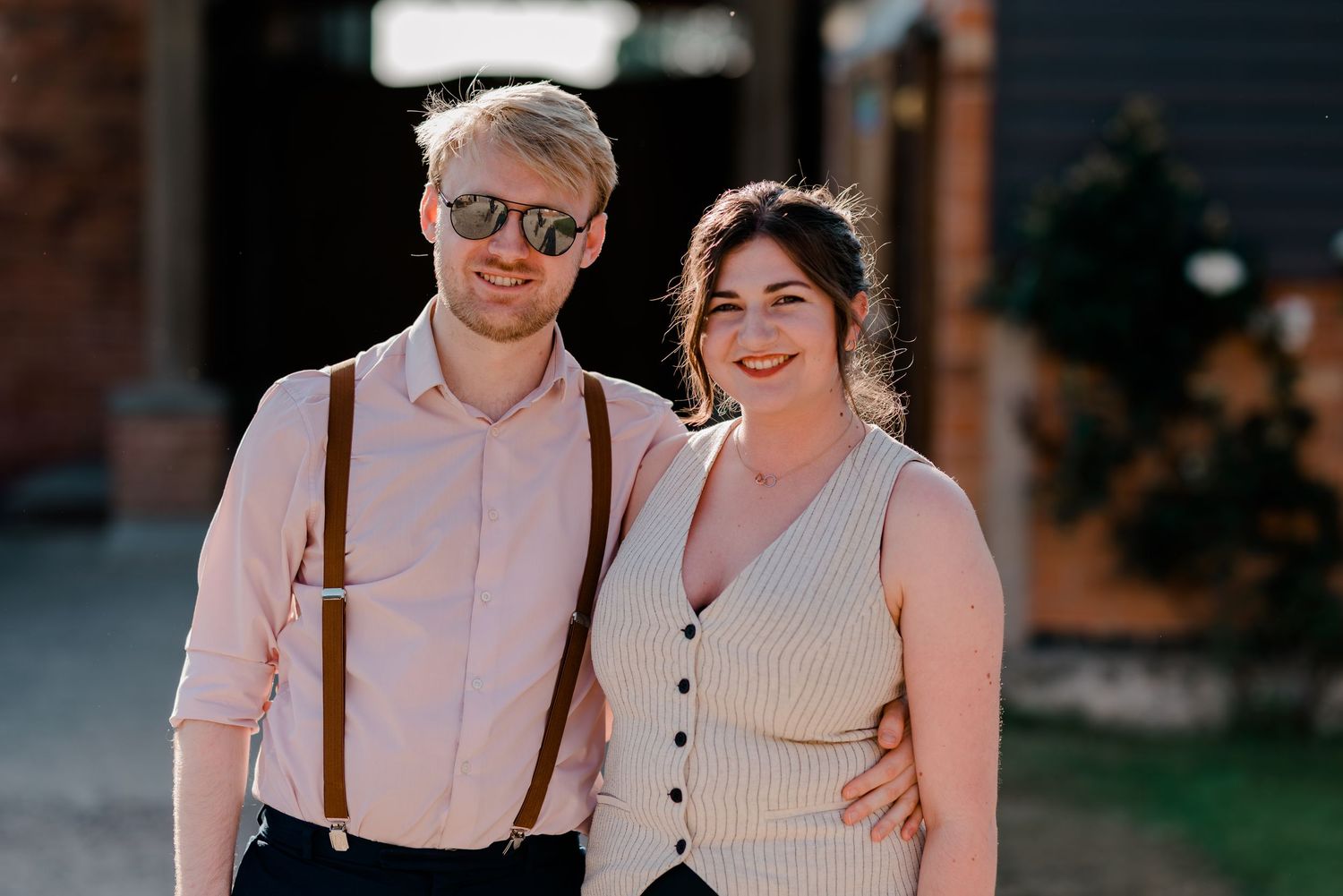 Couple sharing intimate moment in golden sunlight outside brick building.