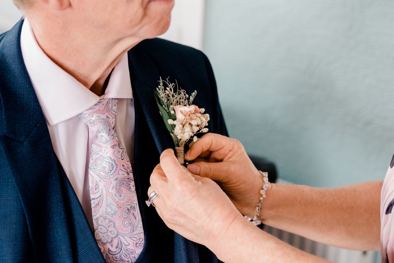Groom at a formal wedding ceremony having boutonniere pinned to his suit lapel.