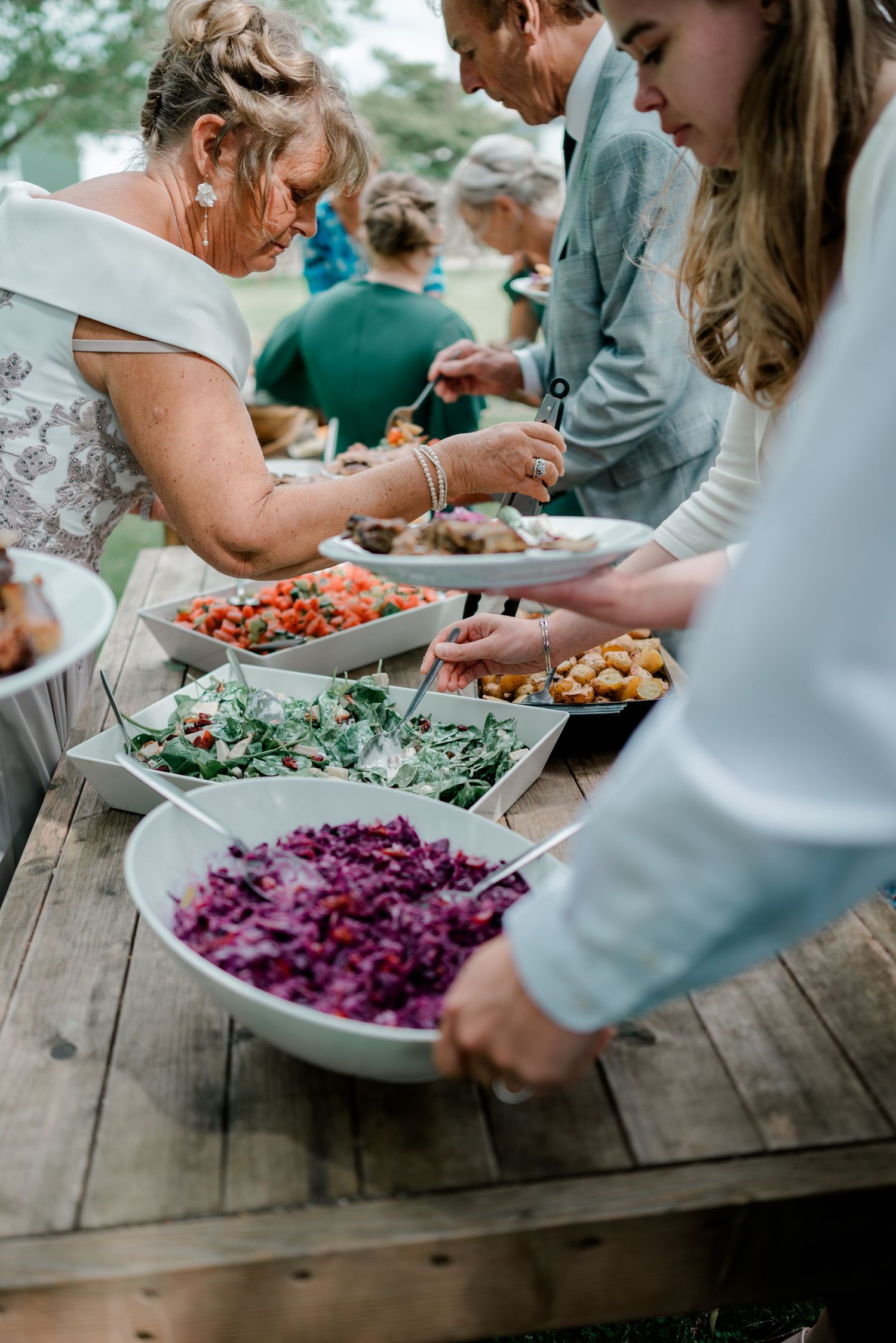 Wedding guests serving themselves at an outdoor buffet table with colorful salads and fresh food dishes.