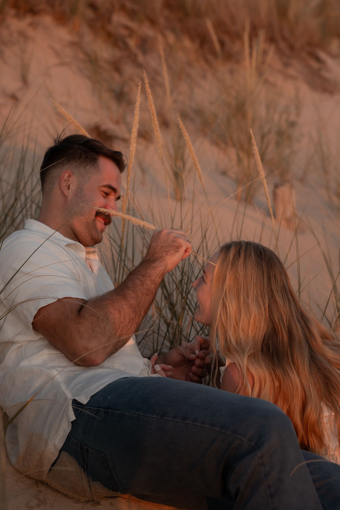 Romantic couple lying in tall grass during golden hour sunset.