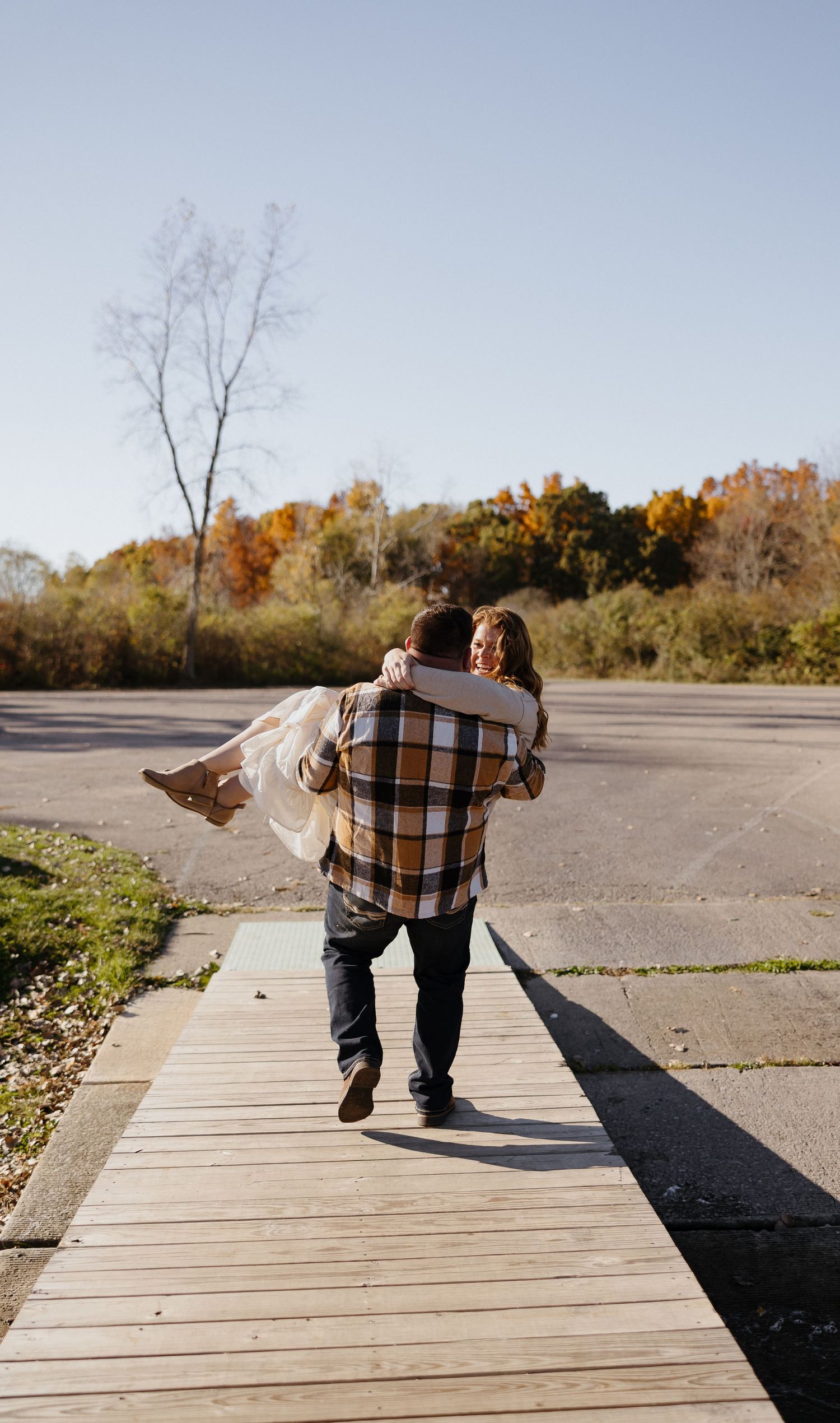 Couple walks together on wooden boardwalk during autumn sunset.
