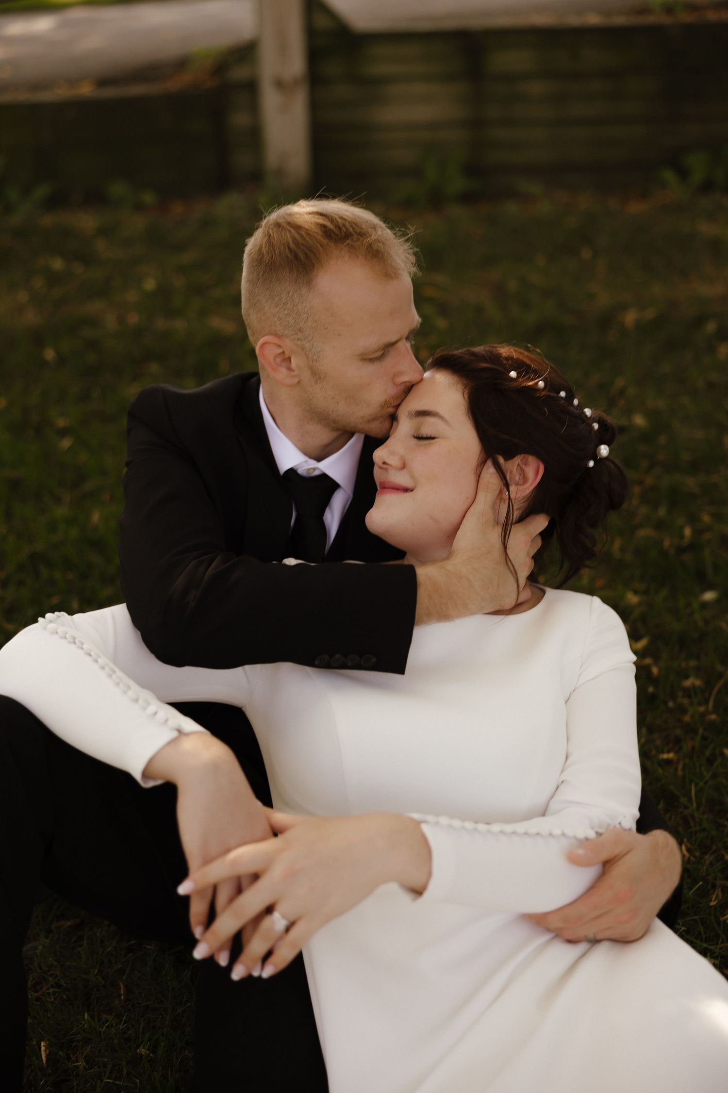 Newlyweds share romantic embraces in their wedding attire outdoors.