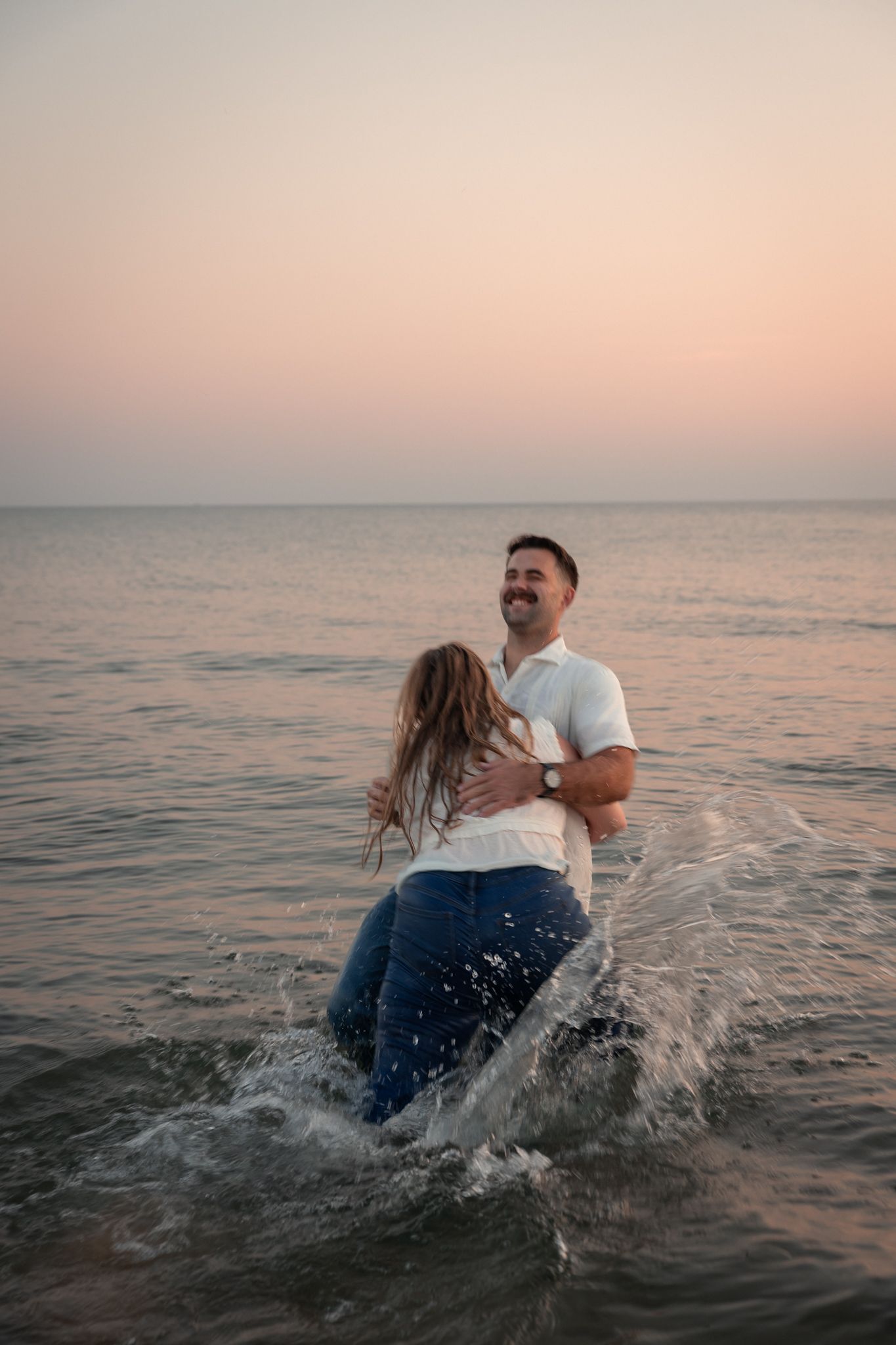 Playful couple splashing in ocean water during sunset.