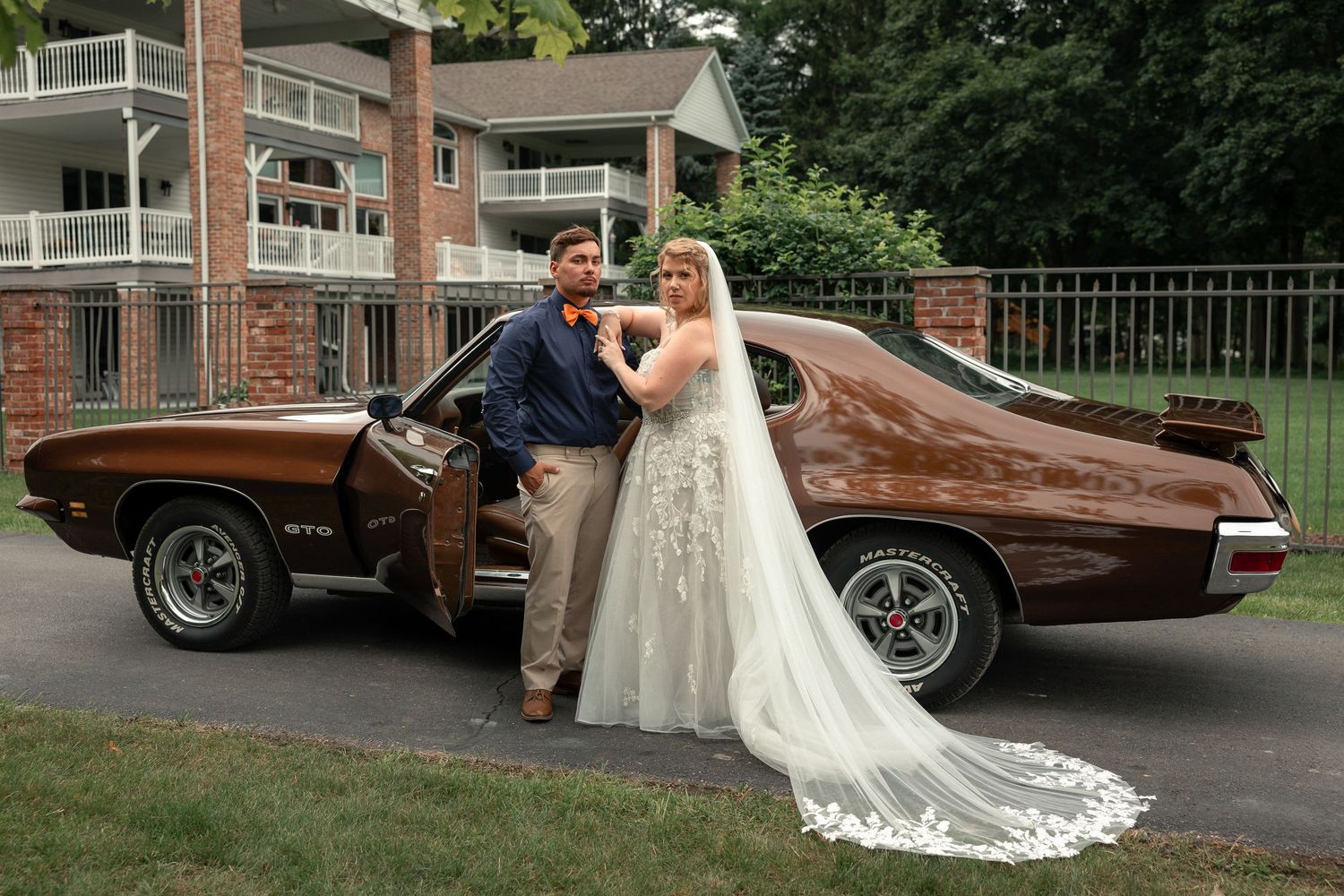 A classic brown vintage car serves as wedding transportation on a tree-lined driveway.