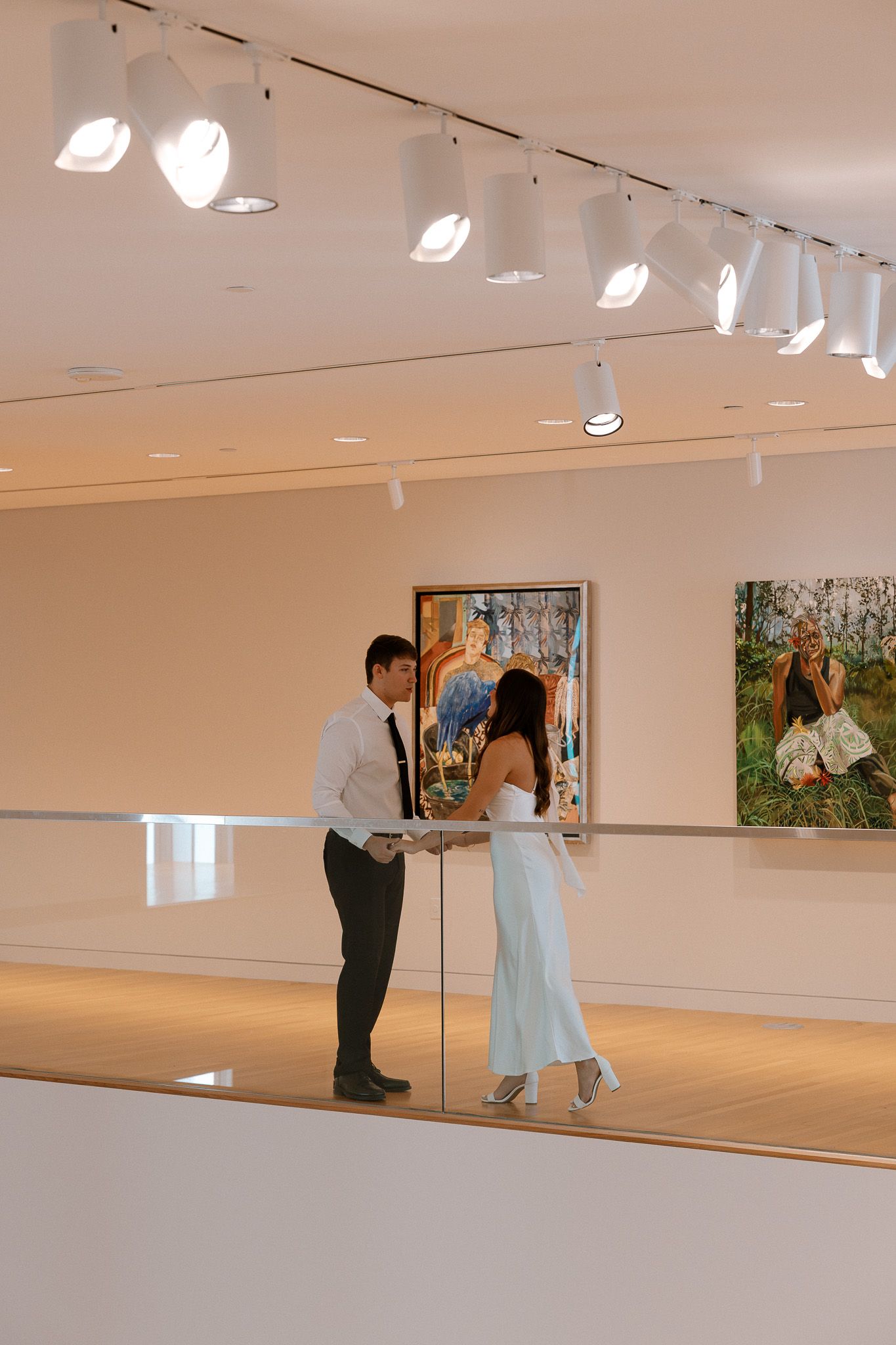 Couple in formal attire sharing a romantic moment in a modern art gallery with track lighting.