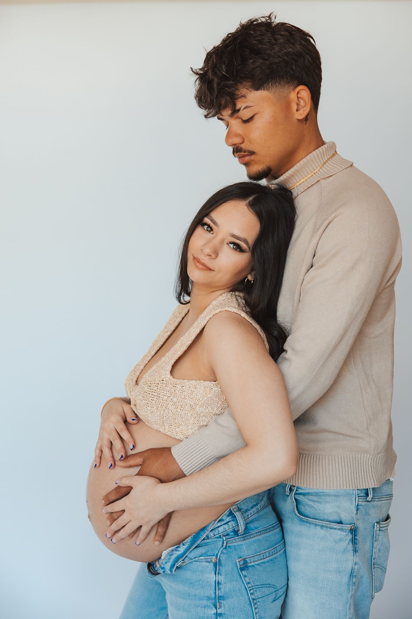 Intimate maternity photos showing couple embracing against light background.
