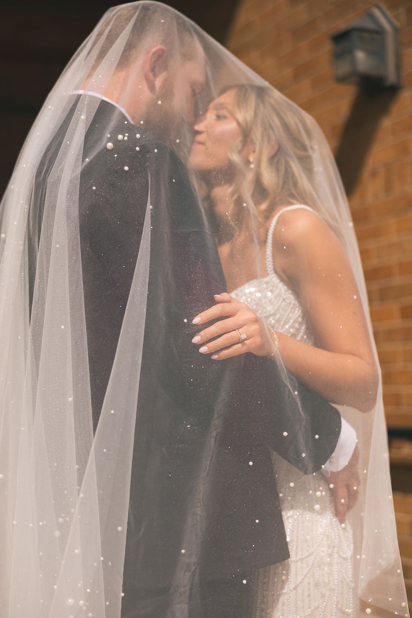 A romantic wedding moment captured as a couple shares a kiss under a delicate white veil at their ceremony.