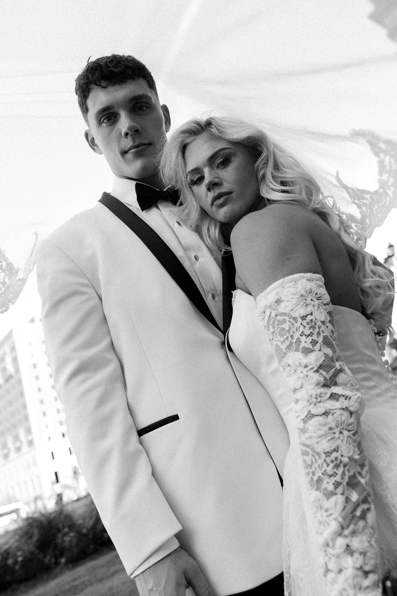 Black and white portrait of elegant bride and groom posing outdoors in wedding attire.