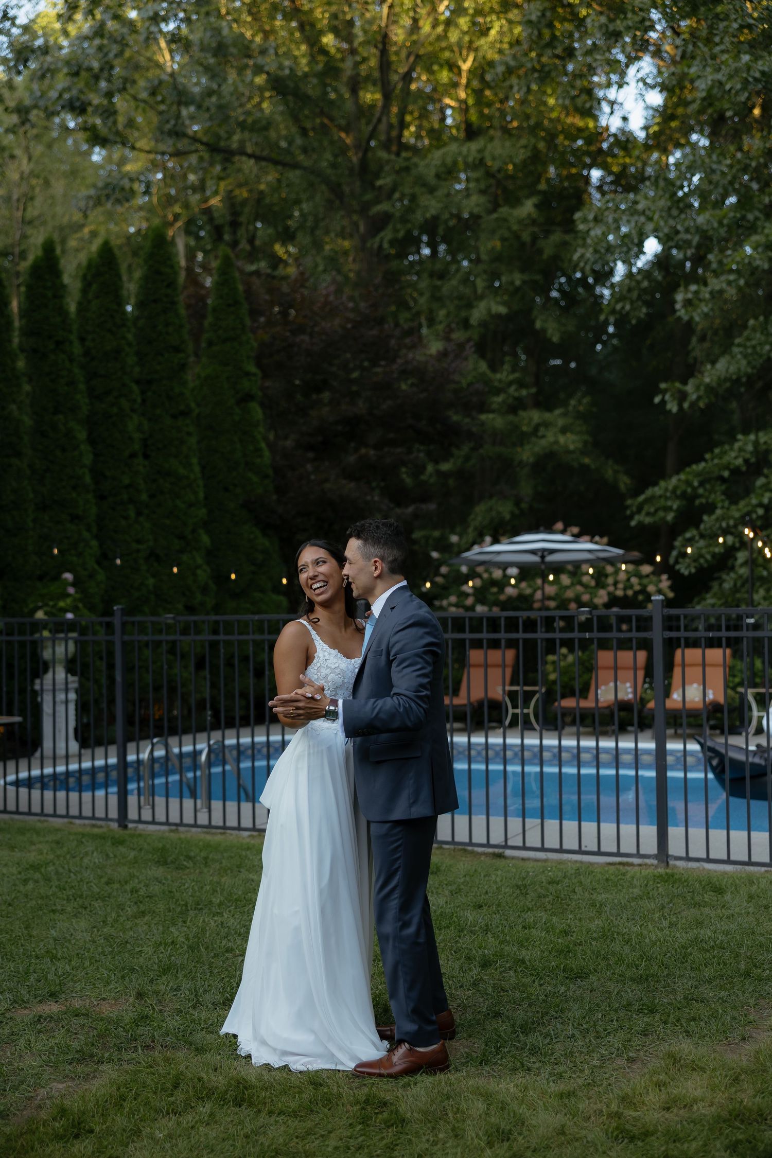 A joyful bride and groom share a romantic moment in a backyard garden near a pool at dusk.