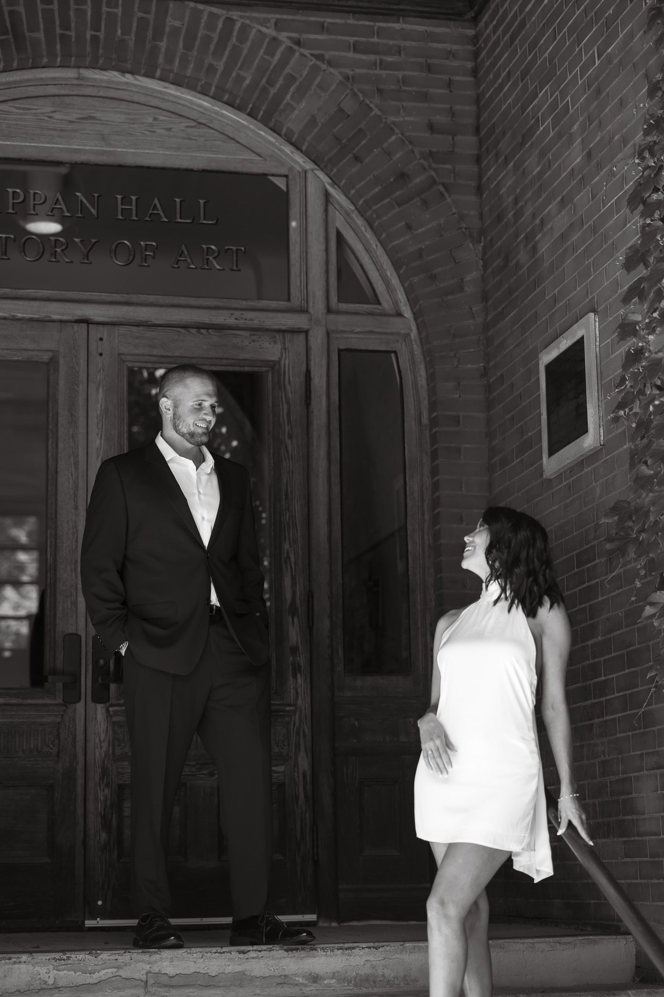 Black and white photo of a couple smiling at each other outside Tappan Hall history of art building.
