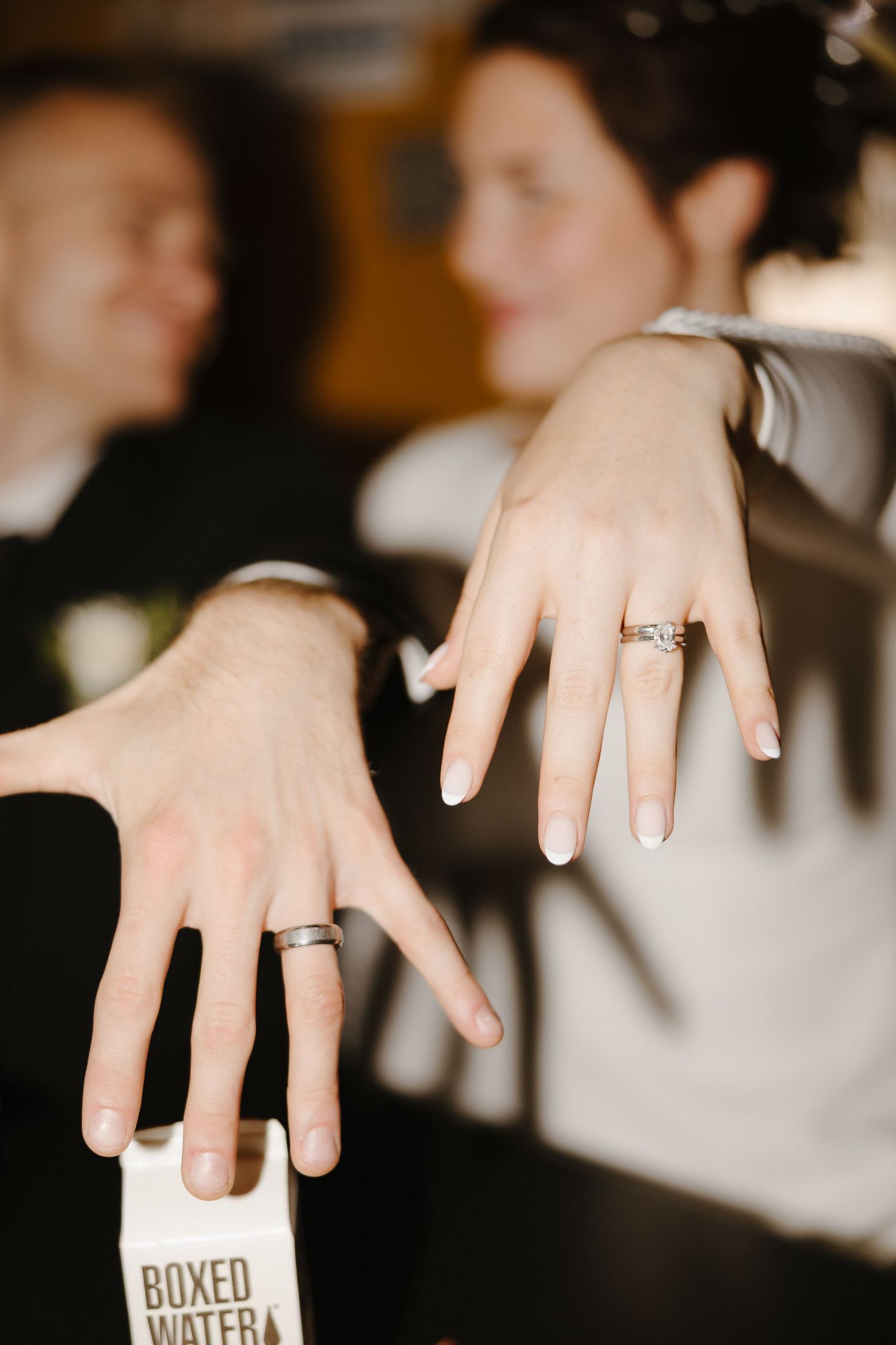 Close up of wedding rings and hands holding boxed water bottles.